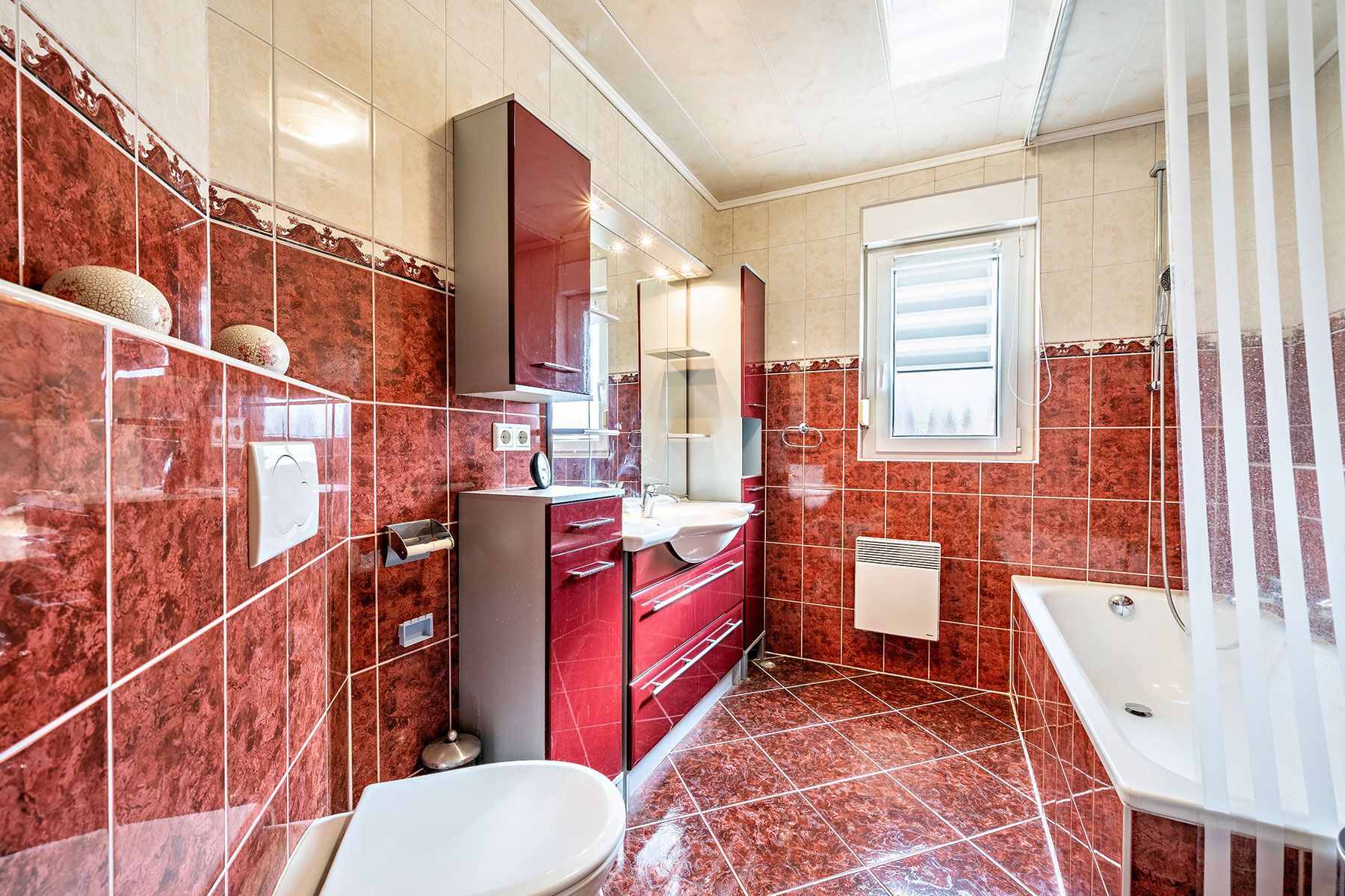 Modernes Badezimmer mit roten Fliesen, Badewanne, Waschbecken, WC und Fenster.