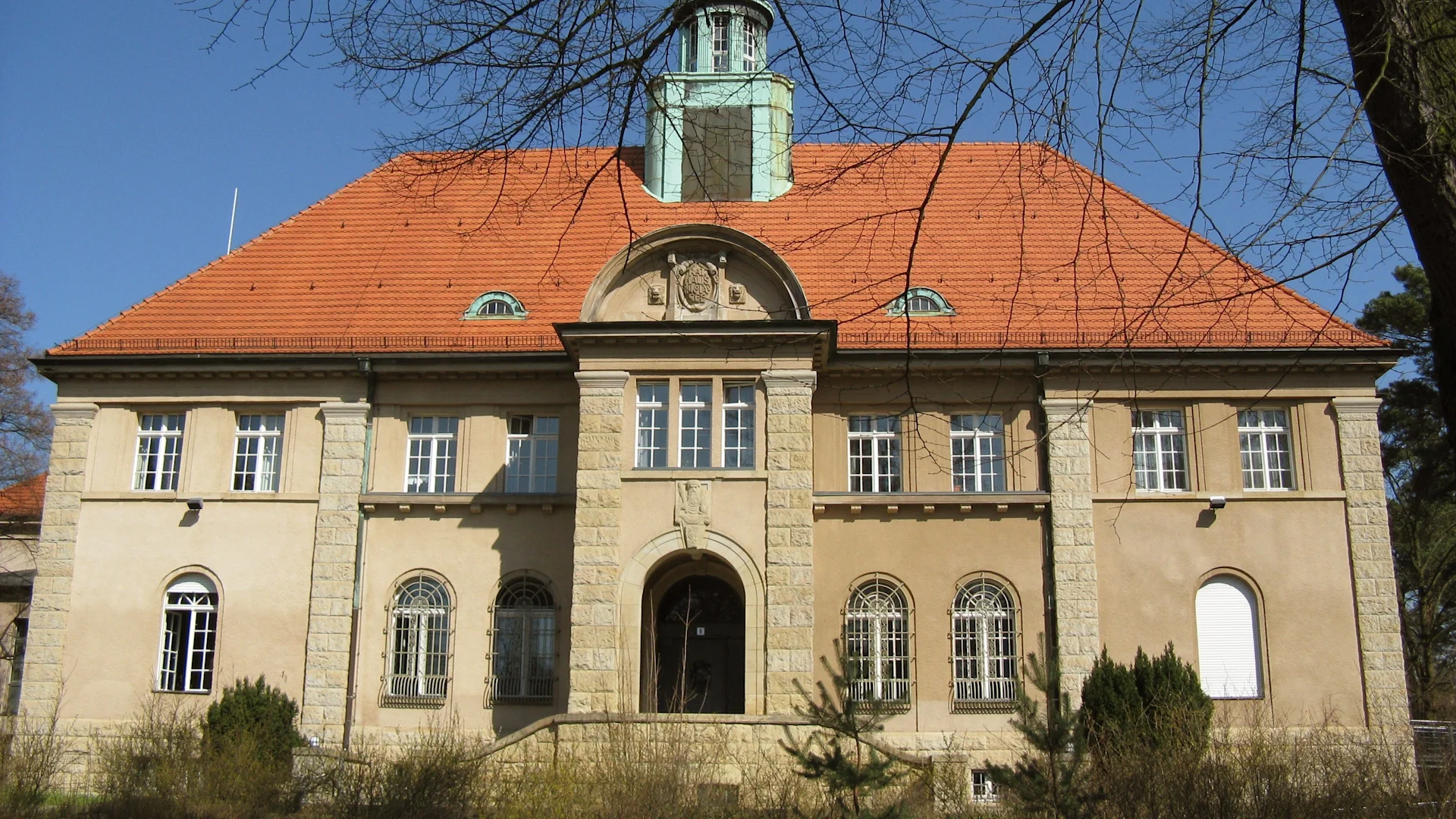 Großes, zweistöckiges Wohnhaus mit rotem Dach, vielen Fenstern und mittlerem Torbogen.