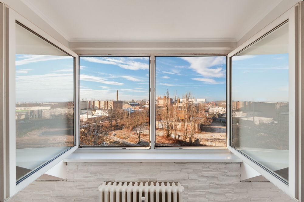 Großes Fenster mit Blick auf städtische Gebäude und blauen Himmel, darunter ein Heizkörper.