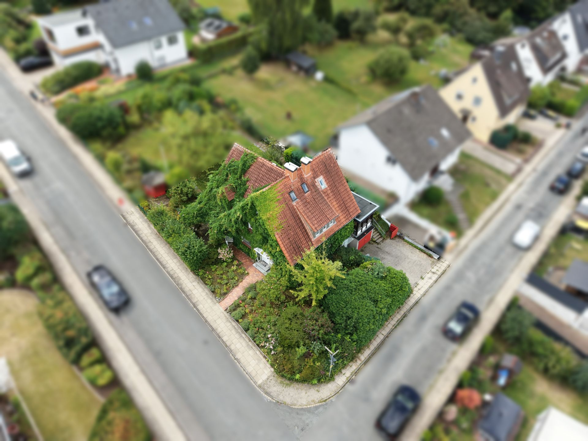 Luftaufnahme eines Einfamilienhauses mit Garten an einer Straßenecke in einem Wohngebiet.