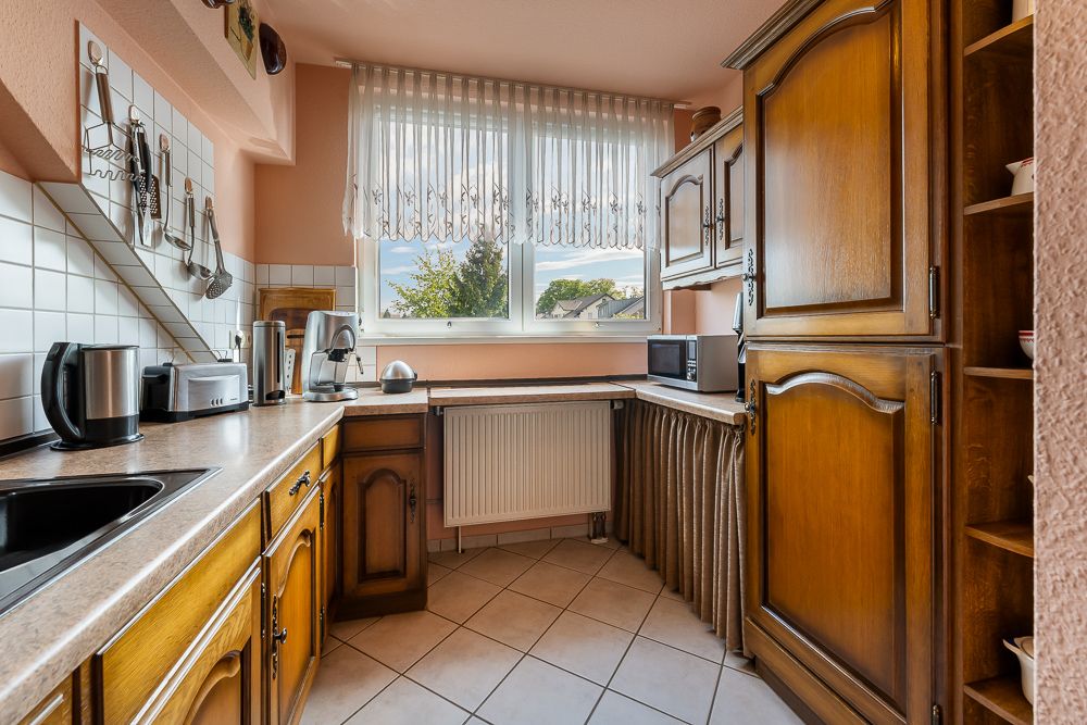 Gemütliche Küche mit Holzschränken, Geräten und großem Fenster mit Vorhängen.