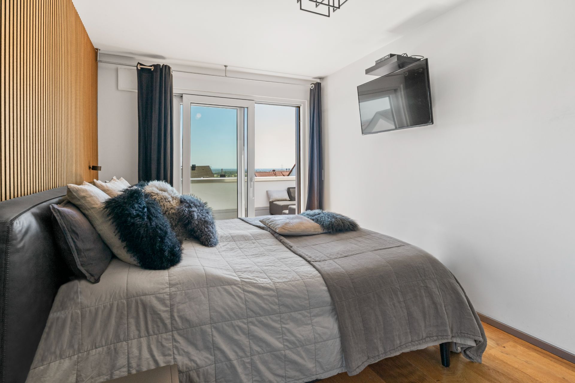 Schlafzimmer mit Doppelbett, Fernseher an der Wand und Zugang zu einem Balkon mit Ausblick.
