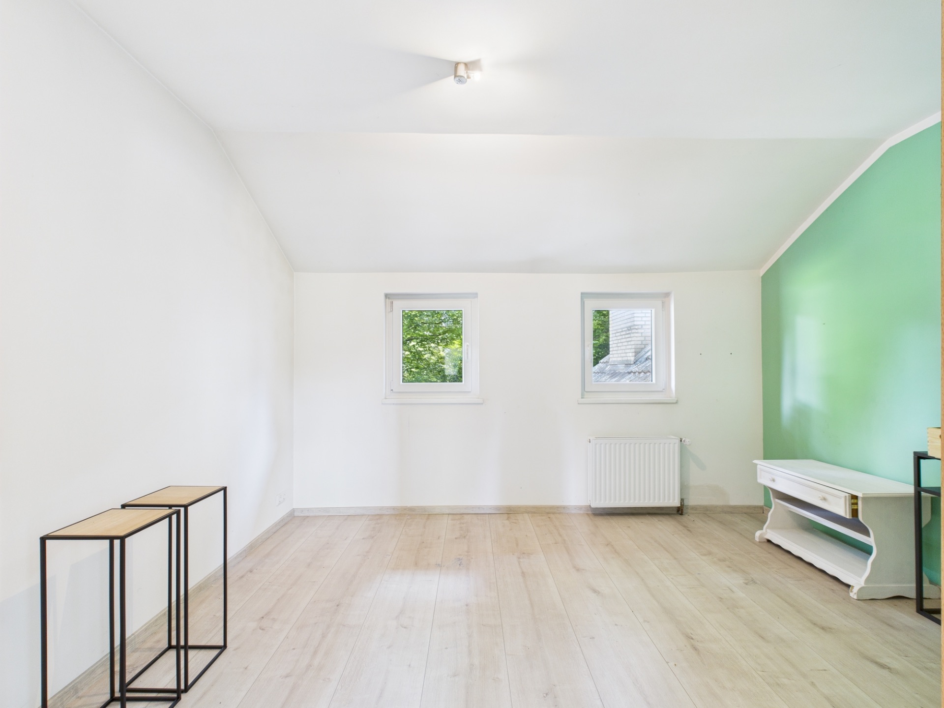 Helles Zimmer mit zwei Fenstern, grün gestrichener Wand und hellen Holzboden.