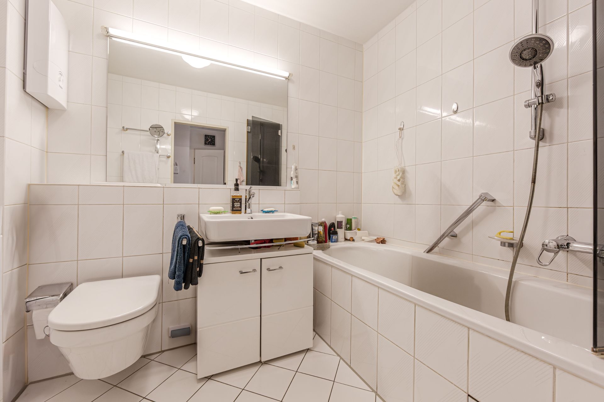 Modernes Badezimmer mit Badewanne, Waschbecken, großem Spiegel und Wandtoilette.
