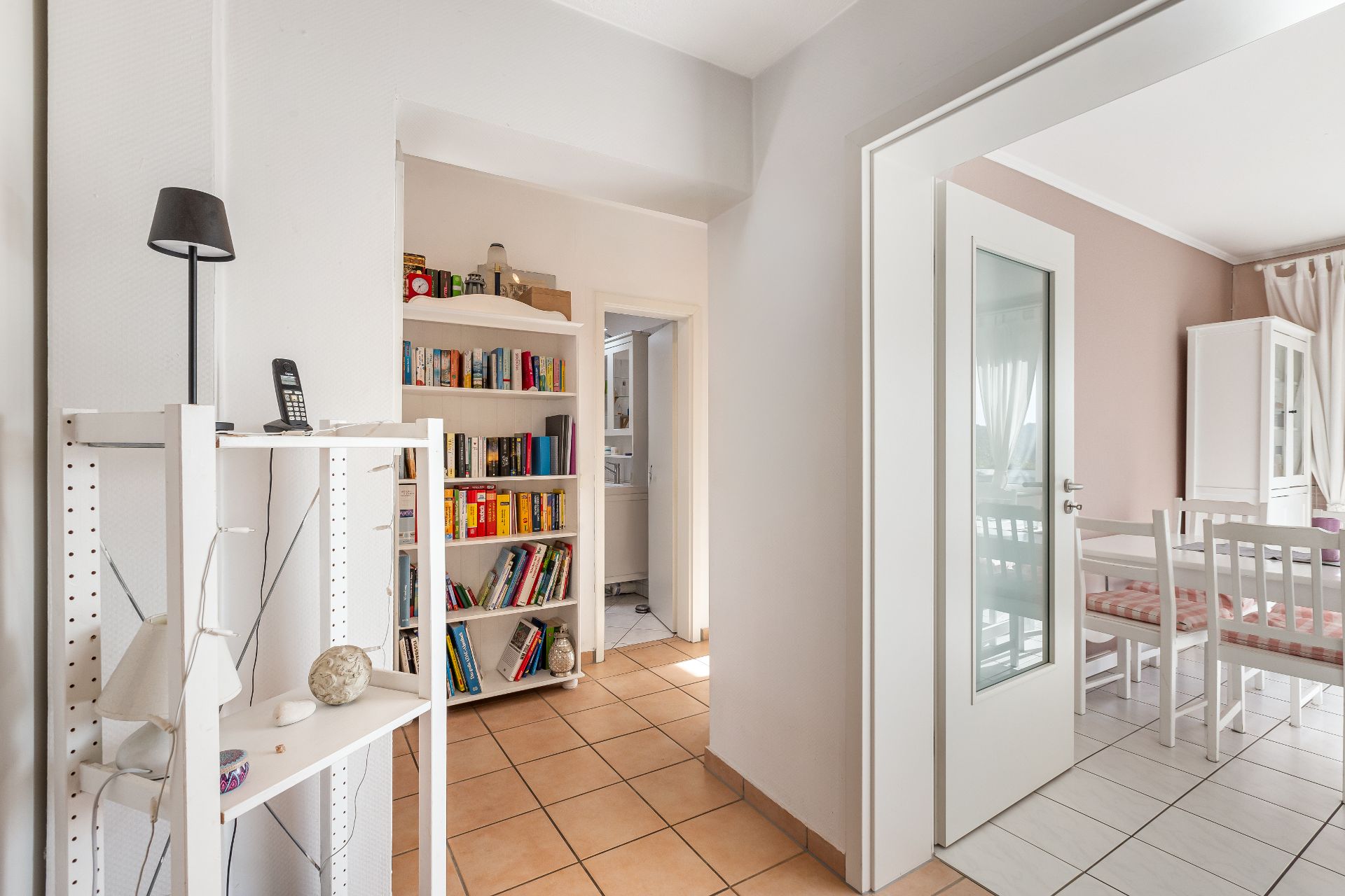 Heller Flur mit Regal, Bücherregal und Blick in ein Esszimmer mit weißen Möbeln.
