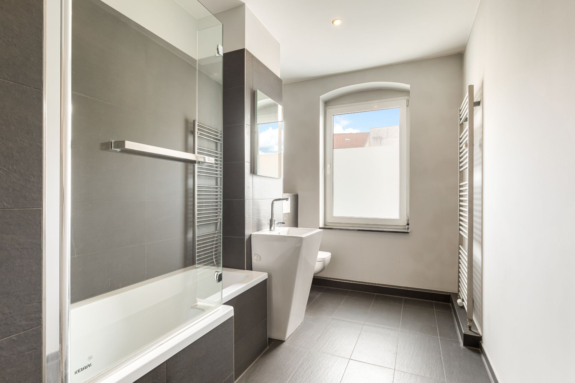 Modernes Badezimmer mit Badewanne, Waschbecken, WC und Fenster.