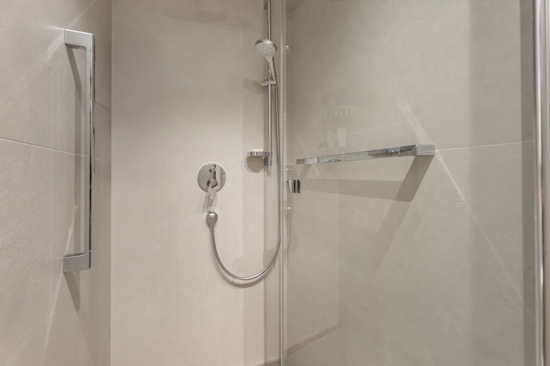 Moderne Dusche mit Glastür und silberner Armatur in einem hell gefliesten Bad.