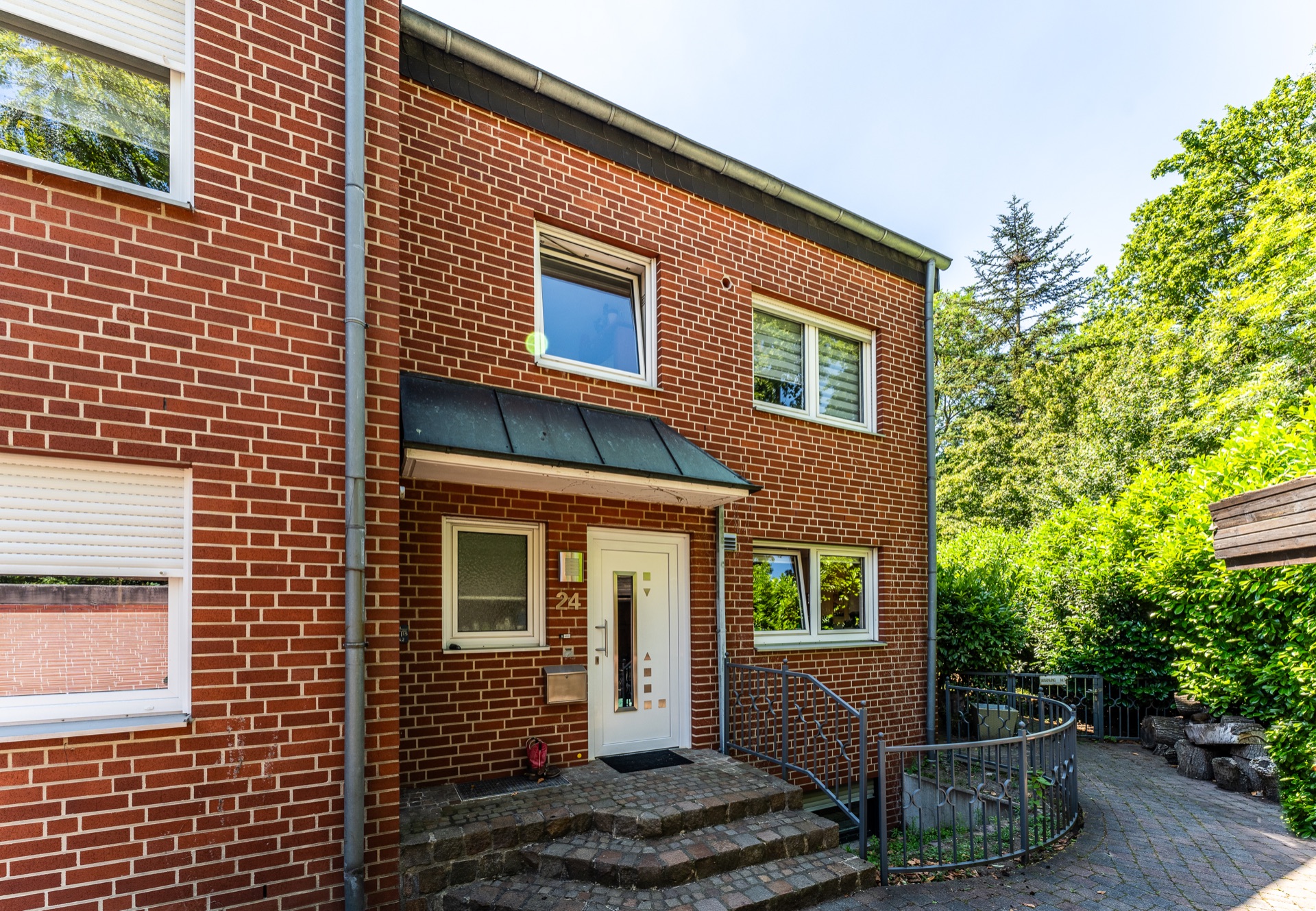 Eingang eines roten Backsteinhauses mit Treppe, weißen Fenstern und Metallgeländer.