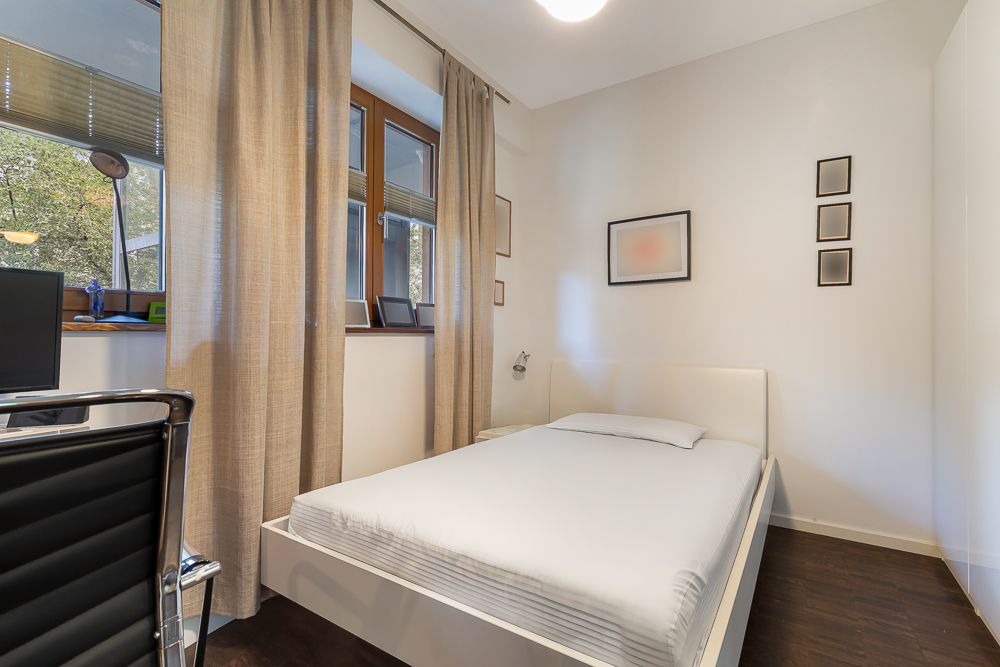 Modernes Schlafzimmer mit Einzelbett, großem Fenster, Schreibtisch und Wandbildern.