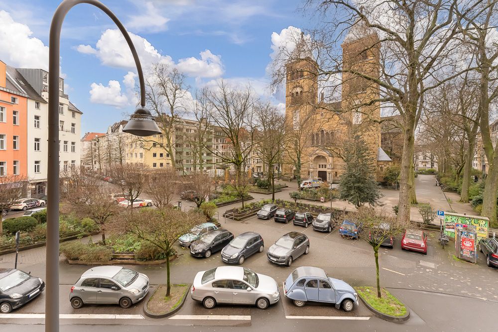 Blick aus dem Fenster auf eine Straße, parkende Autos und eine große Kirche mit zwei Türmen.