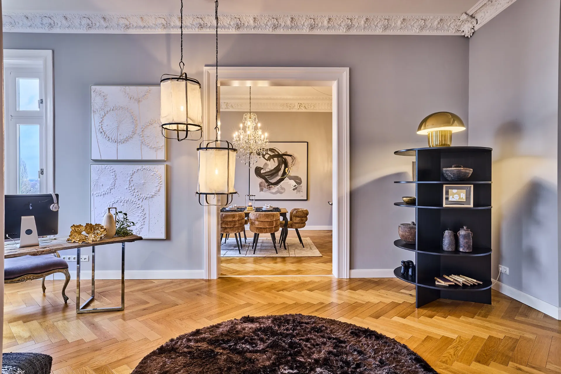 Helles Wohnzimmer mit Schreibtisch, runder Teppich, Regal und Blick in ein Esszimmer mit Kronleuchter.
