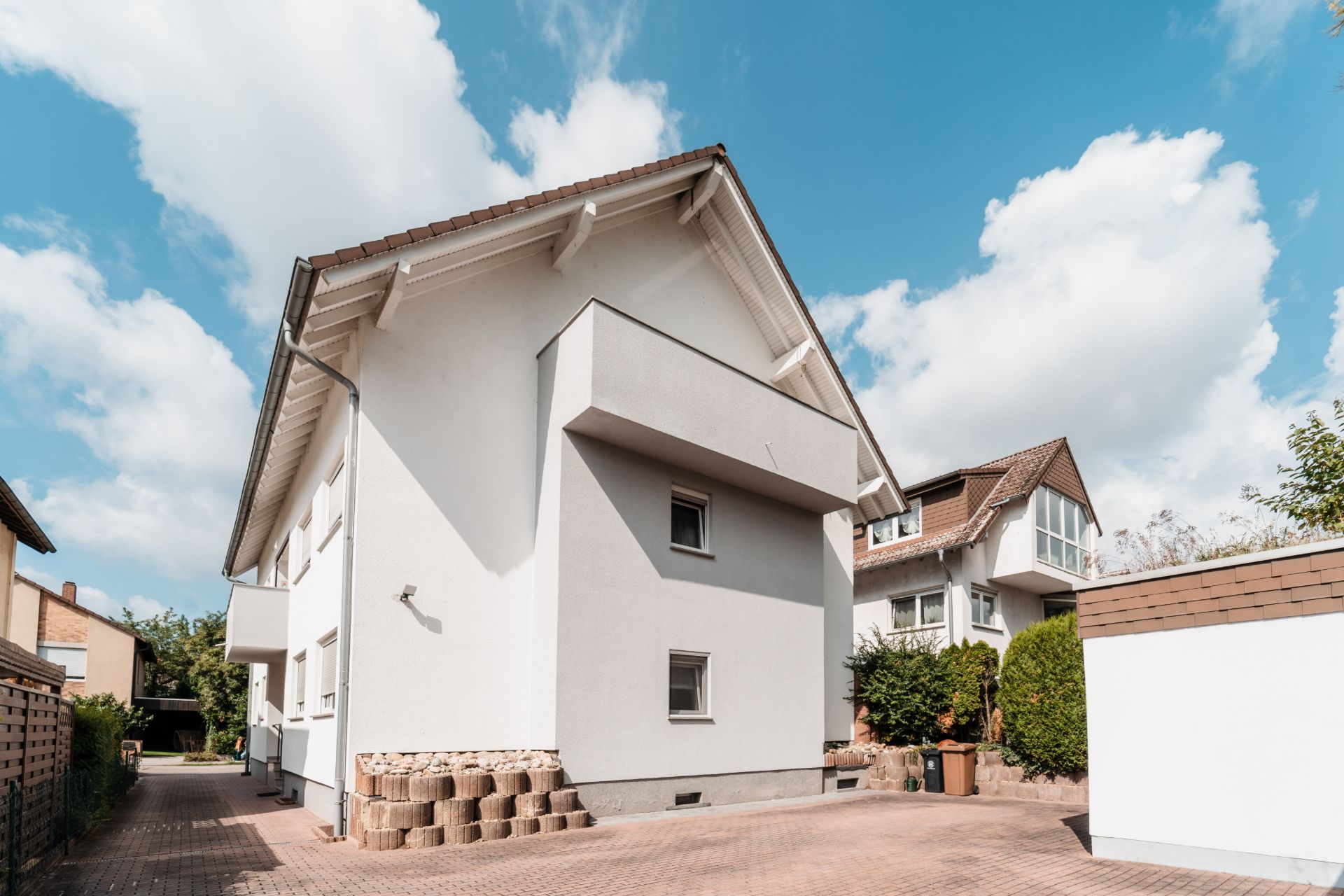 Modernes weißes Wohnhaus mit Satteldach und Balkon, aufgenommen an einem sonnigen Tag.