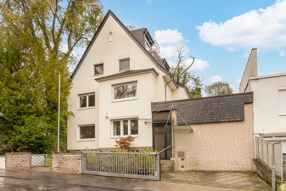 Modernes, dreistöckiges Wohnhaus mit Satteldach und kleinem Vorgarten, umgeben von Bäumen.