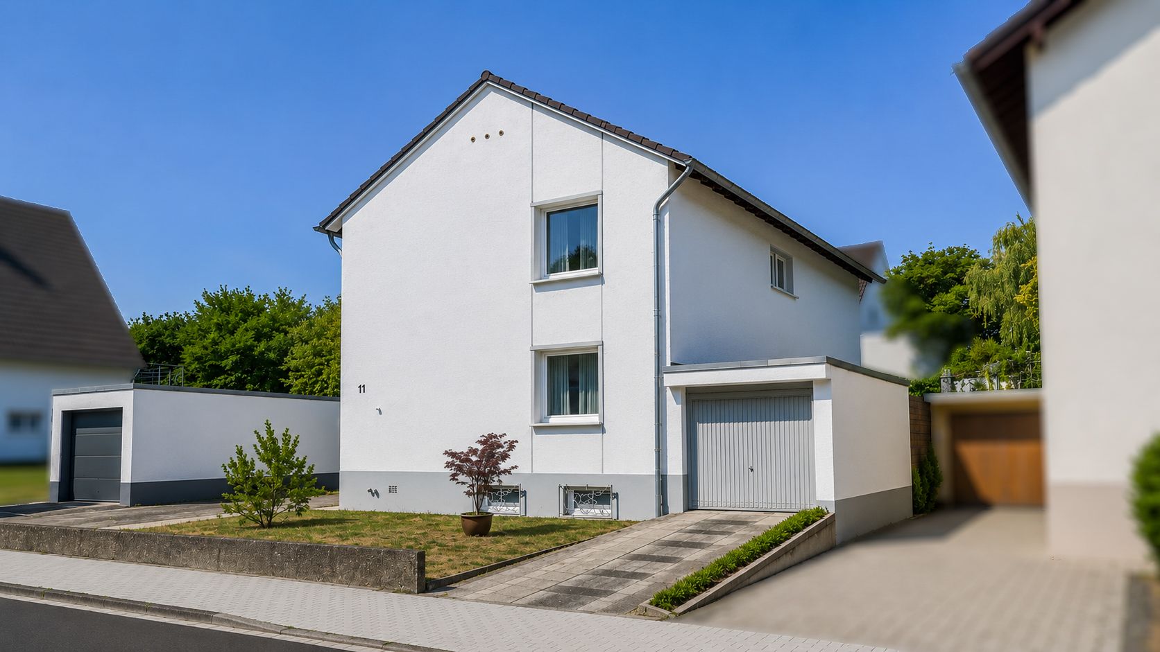 Modernes weißes Wohnhaus mit Garage und kleinem Vorgarten an einer ruhigen Straße.