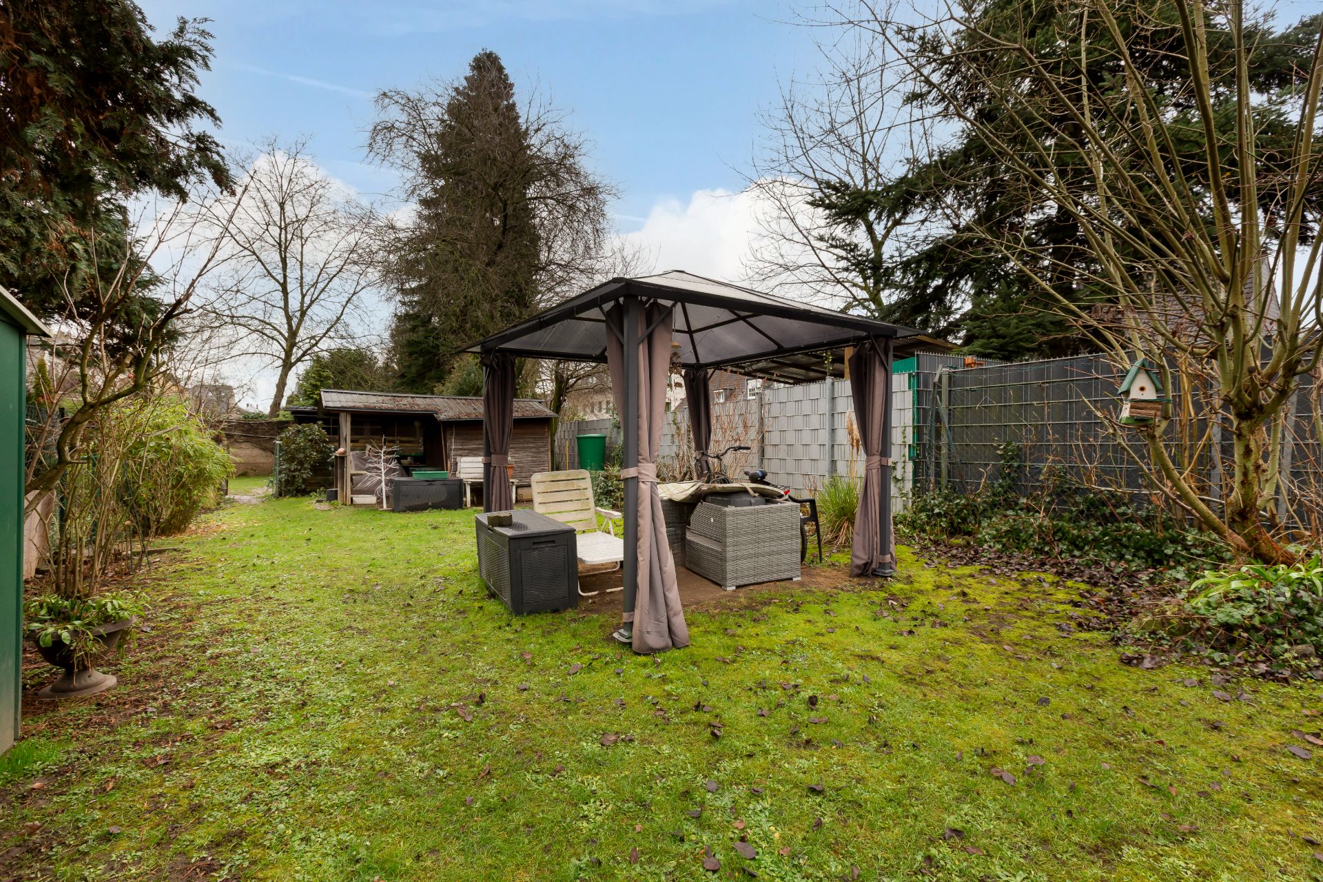Garten mit Pavillon, Gartenmöbeln und Sitzbereich, umgeben von Bäumen und Sträuchern.