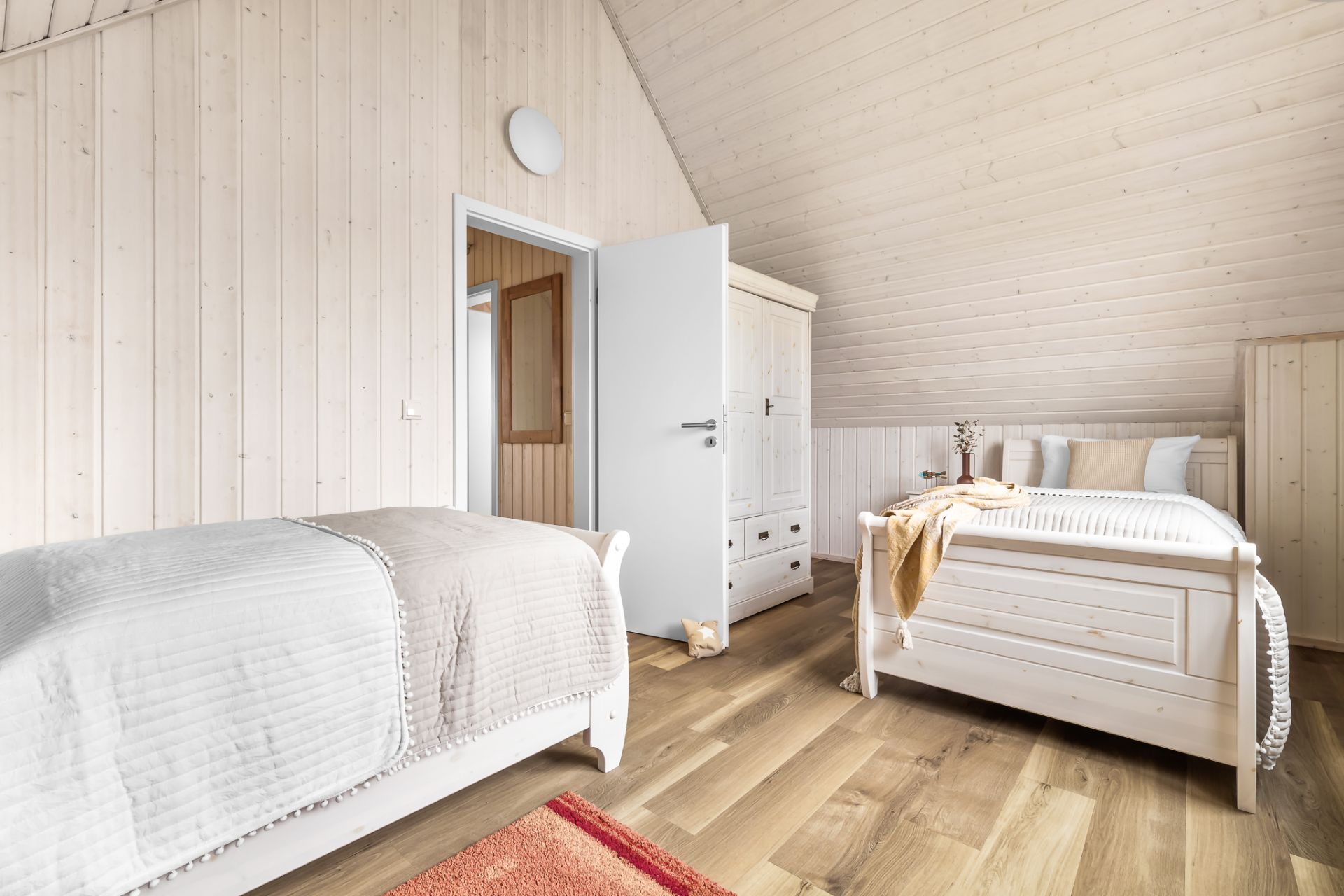 Helles Schlafzimmer mit zwei Einzelbetten, Holzfußboden und einem weißen Kleiderschrank.