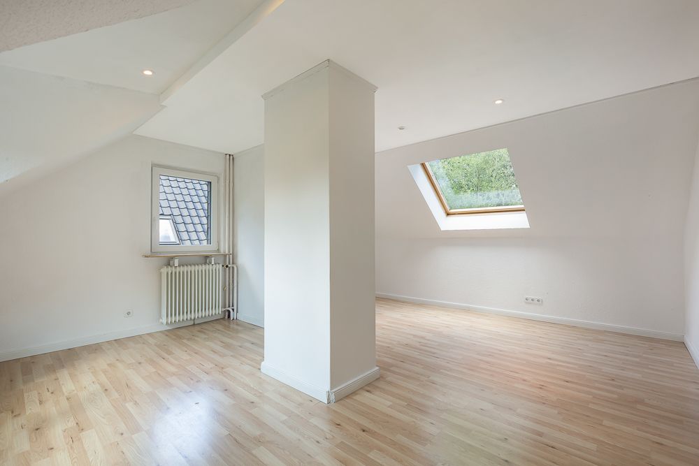 Helles Dachzimmer mit Holzfußboden, Dachfenster und Heizkörper an der Wand.