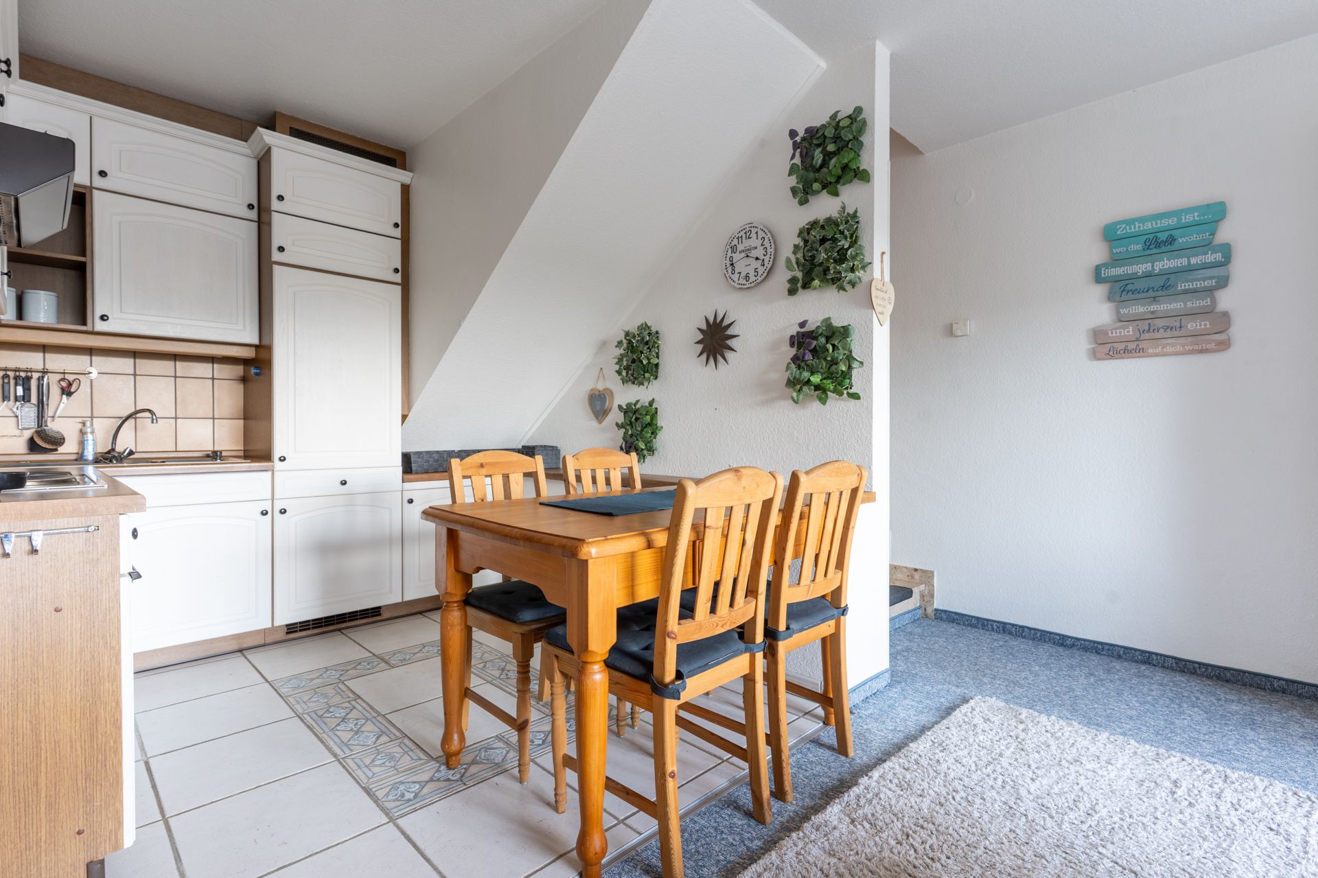 Essbereich mit Holztisch und vier Stühlen neben einer weißen Einbauküche unter einer schrägen Wand.