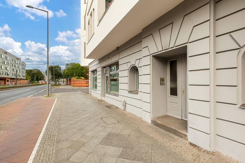 Eingang eines Wohnhauses mit grauer Fassade, Gehweg und Straße daneben.