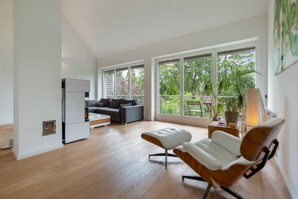 Helles Wohnzimmer mit Holzfußboden, Sessel, Sofa, großen Fenstern und Blick auf den Garten.