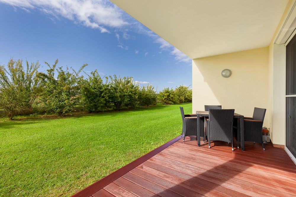 Überdachte Terrasse mit Holzboden, Esstisch und Stühlen, Blick auf Rasen und Büsche.