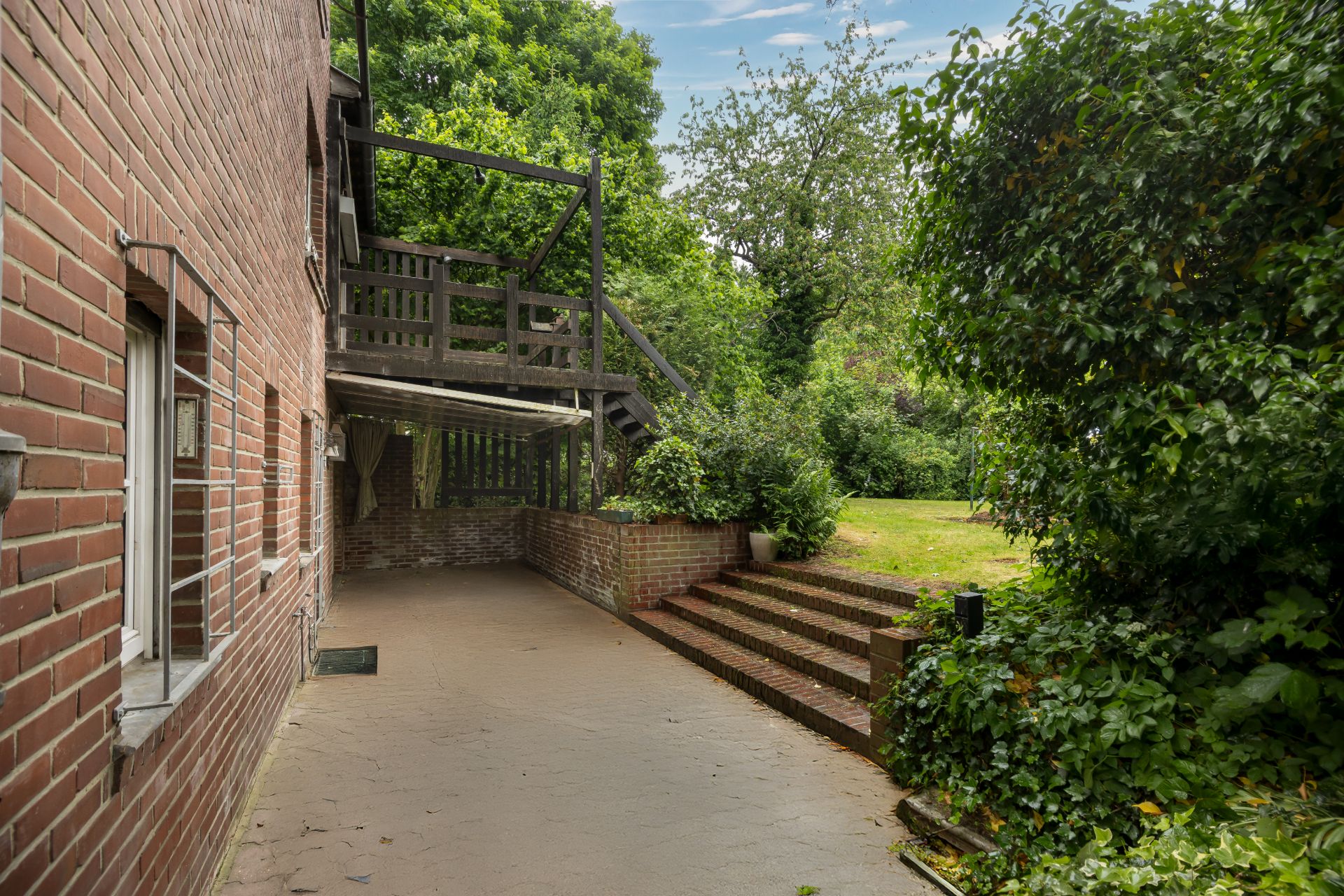 Ziegelhof mit Terrasse, Treppe und viel grünem Garten im Hintergrund.