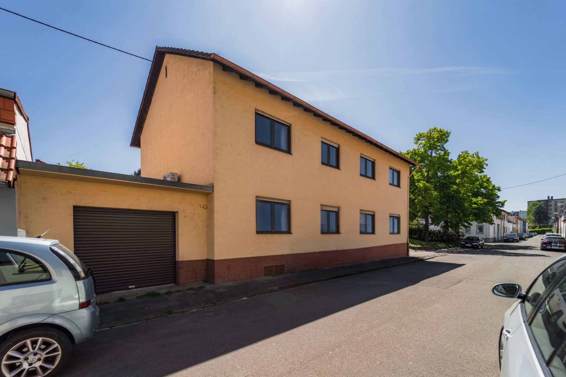 Gelbes zweistöckiges Wohnhaus mit braunem Garagentor an einer ruhigen Straße.