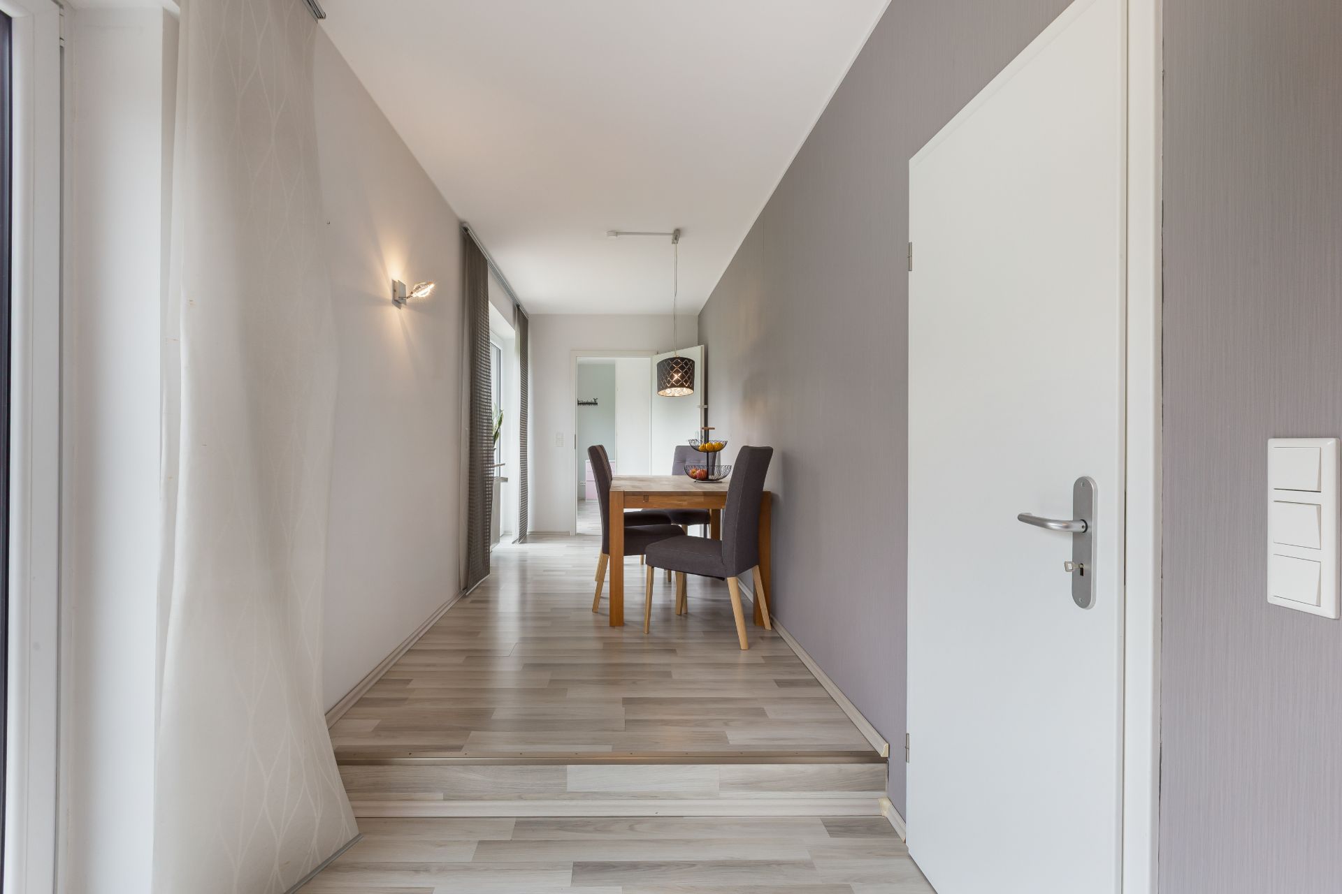 Heller Flur mit Holzboden, Esstisch und Stühlen im Hintergrund.