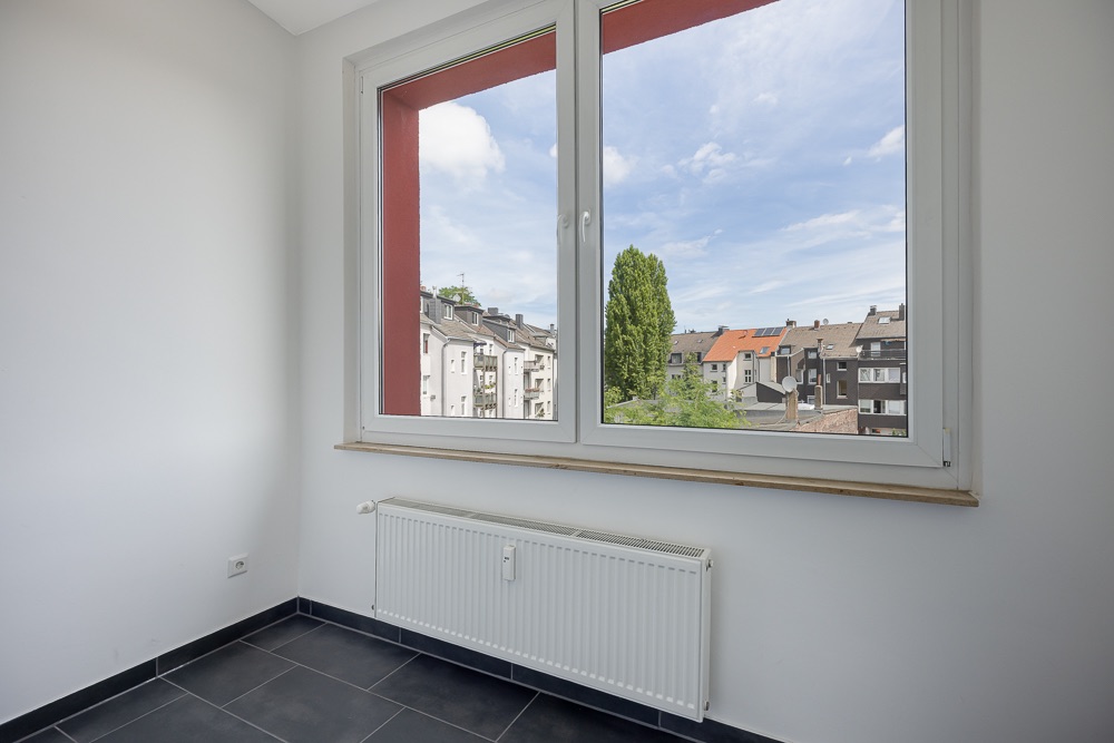 Helles Zimmer mit großem Fenster, Blick auf Nachbarhäuser, unter dem Fenster ein Heizkörper.