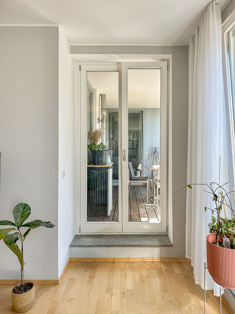 Helles Wohnzimmer mit Holzboden, großen Fenstertüren und mehreren Zimmerpflanzen.