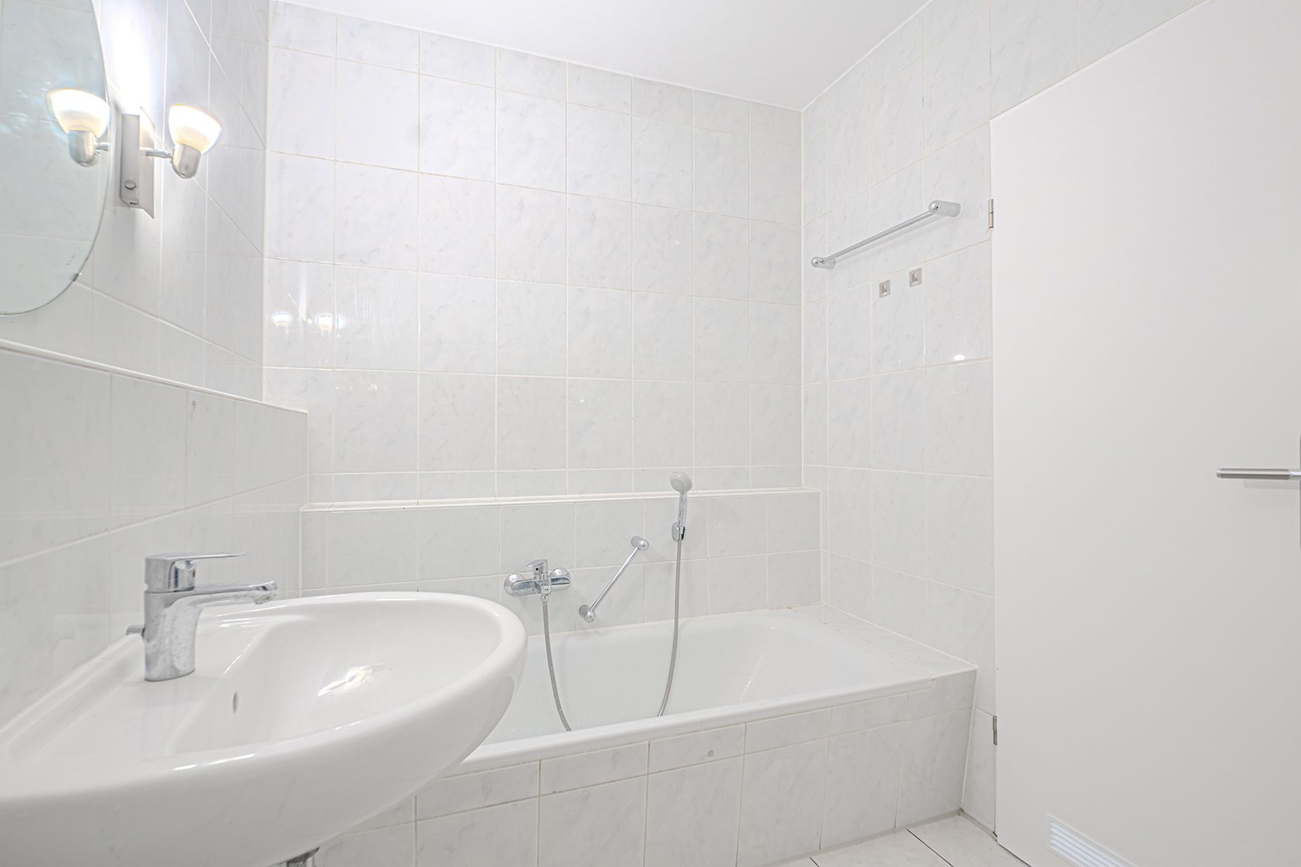 Helles Badezimmer mit Badewanne, Waschbecken und weiß gefliesten Wänden.