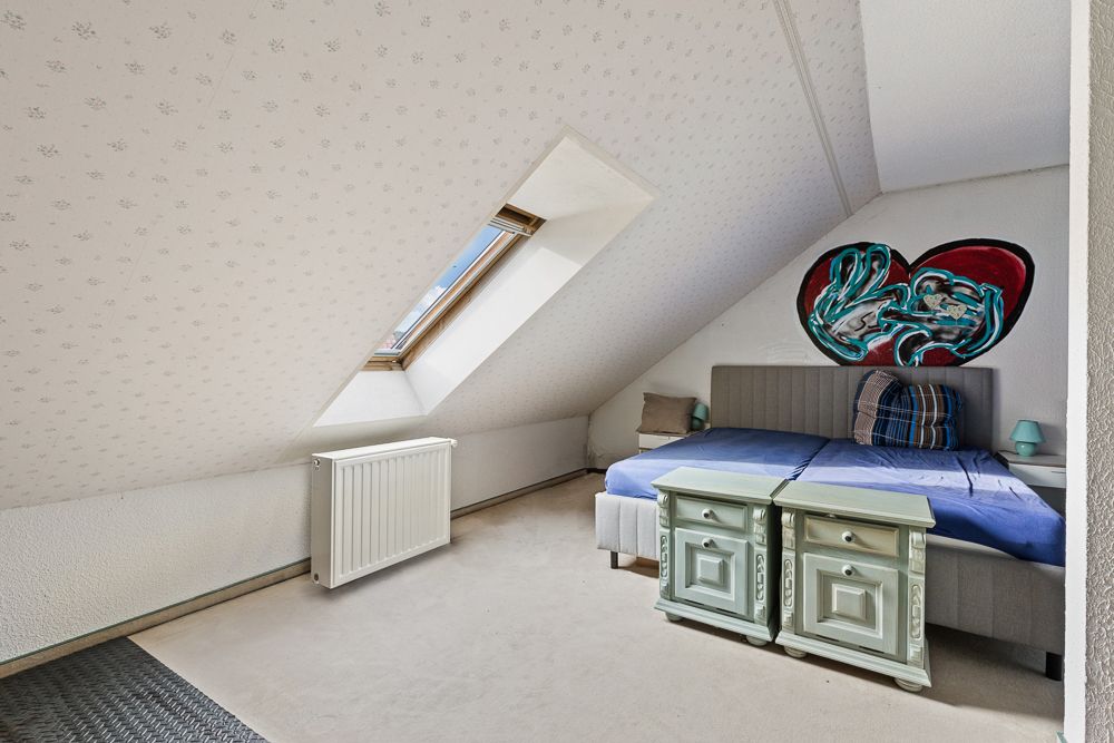 Dachzimmer mit Bett, zwei Nachttischen, Dachfenster und Wandbild in Herzform.