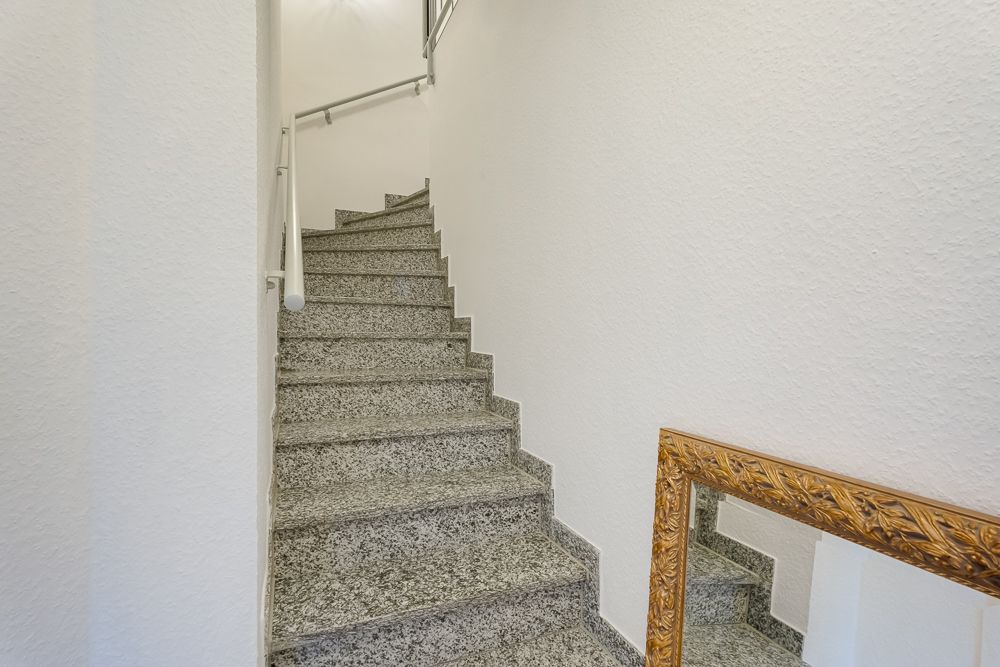 Graue Steintreppe mit weißem Geländer und goldgerahmtem Spiegel an der Wand.