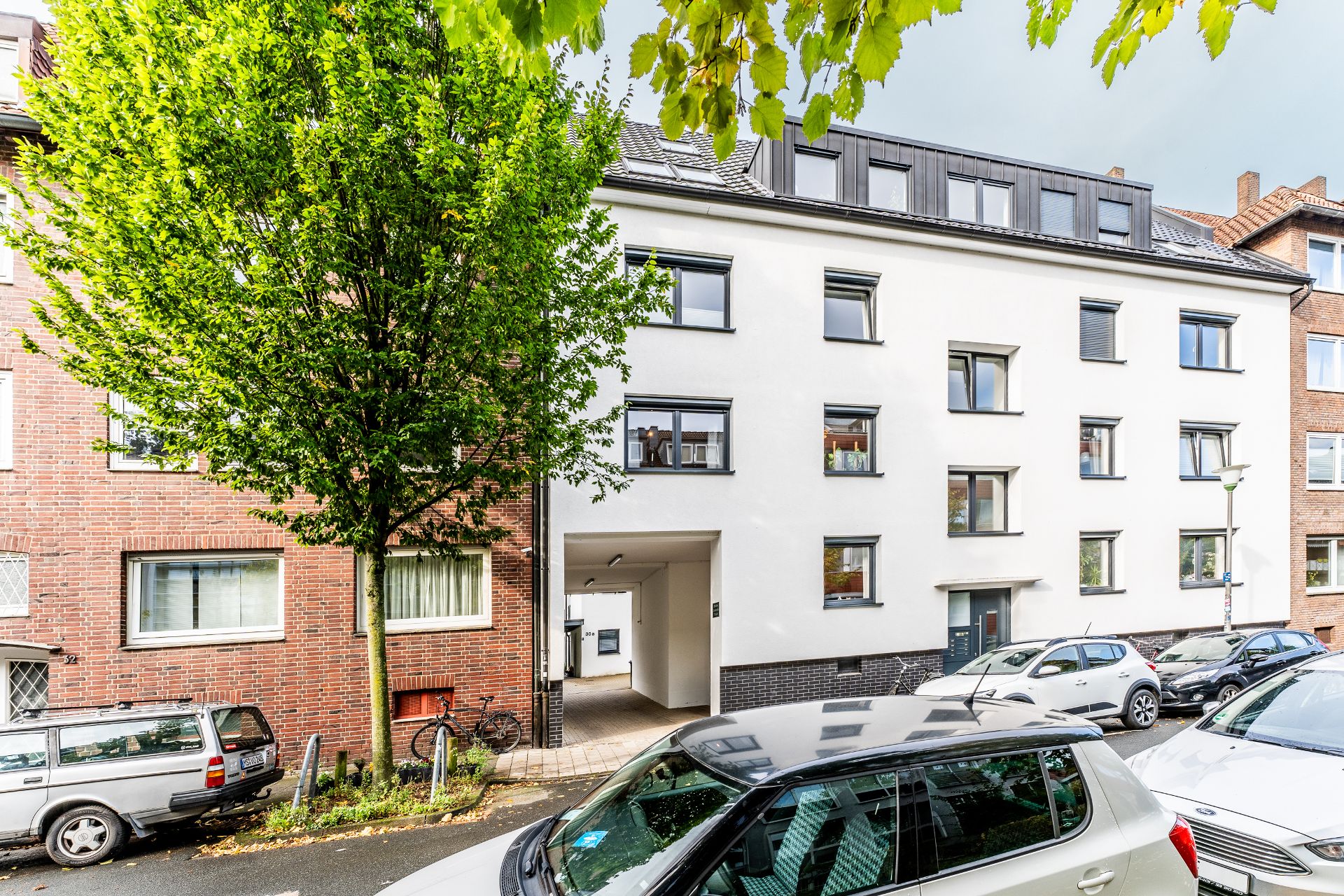 Mehrfamilienhaus mit weißer Fassade, mehreren Fenstern und geparkten Autos davor.