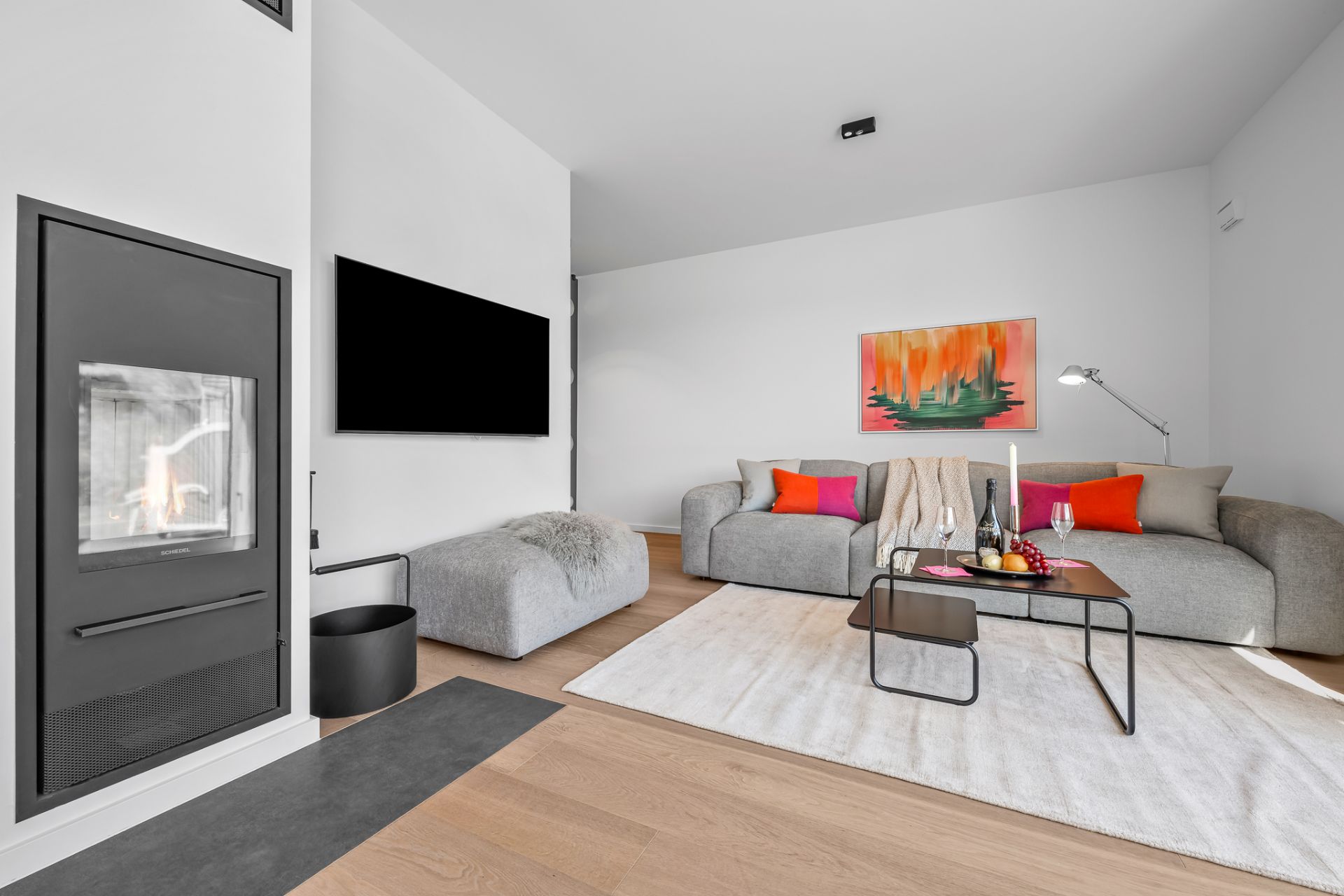 Modernes Wohnzimmer mit Kamin, Fernseher, grauen Sofas, Couchtisch und buntem Wandbild.