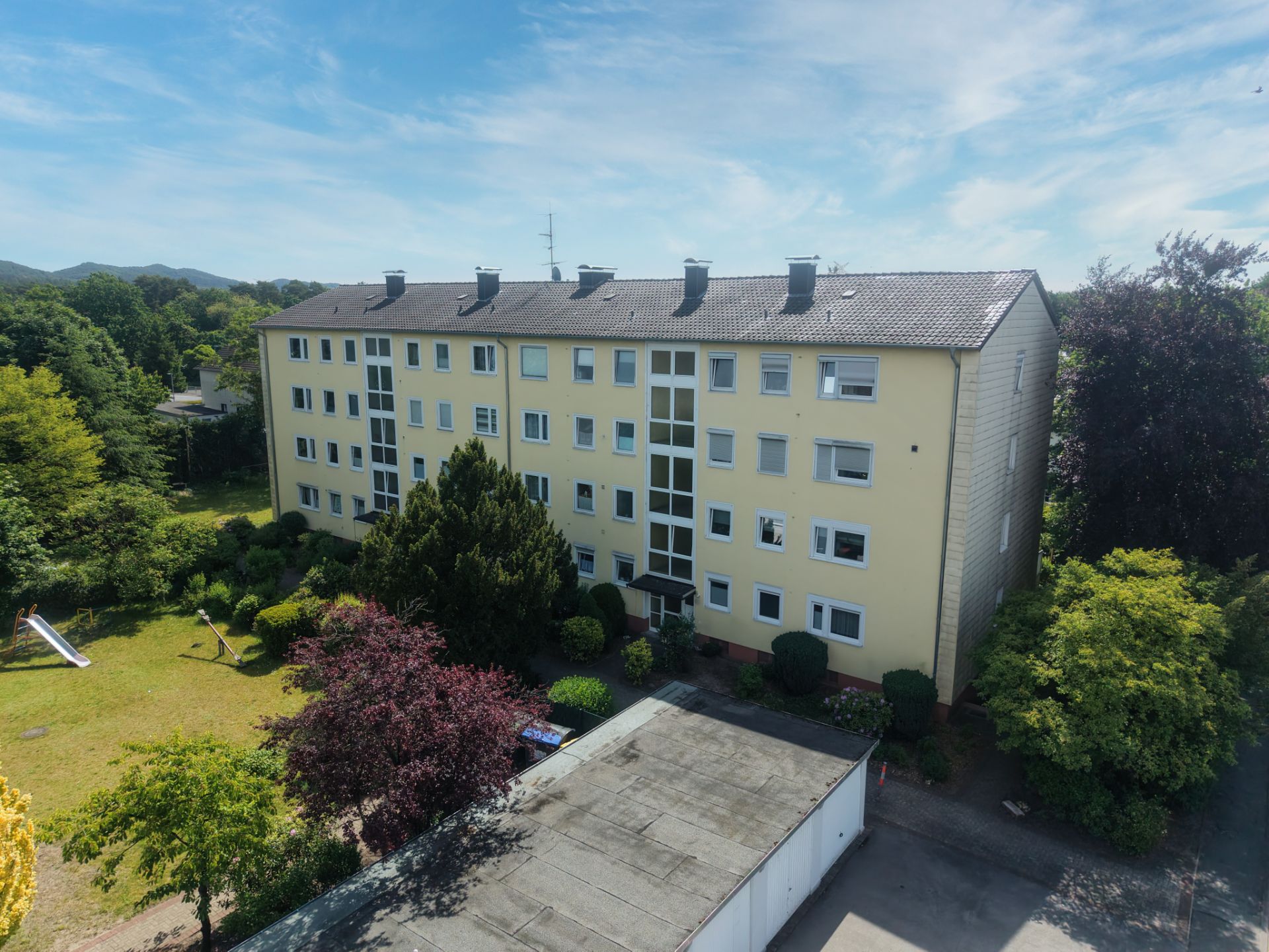 Mehrfamilienhaus mit vier Etagen, umgeben von Bäumen und einem Gartenbereich.