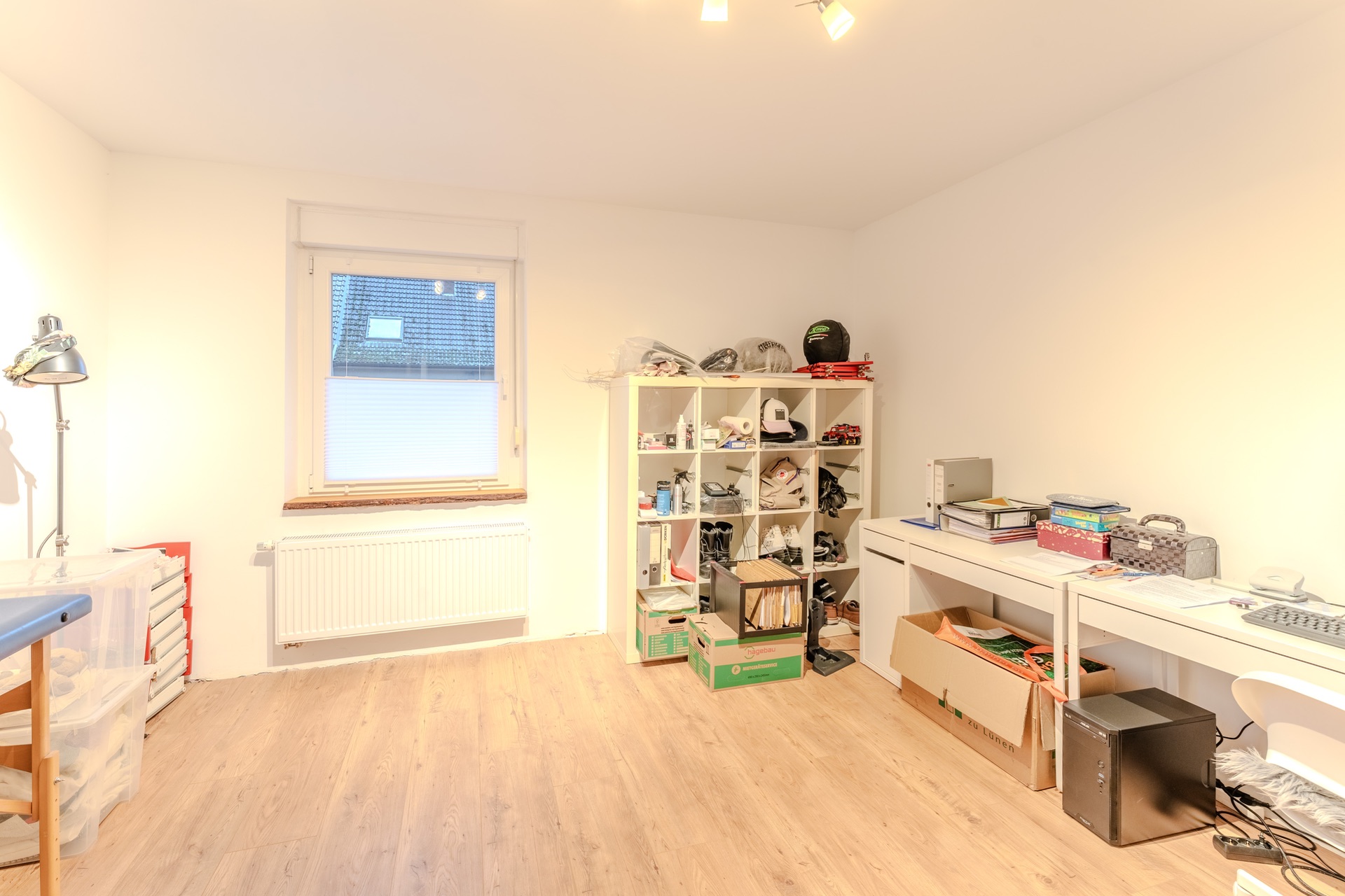 Helles Arbeitszimmer mit Regal, Schreibtisch und Kartons auf hellem Holzboden.