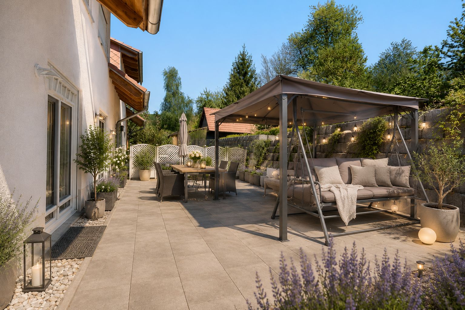 Moderne Terrasse mit Schaukelsofa, Esstisch, Pflanzen und Lichtern im Garten eines Wohnhauses.