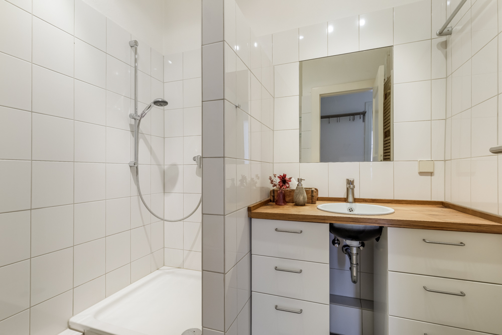 Modernes Bad mit Dusche, Waschbecken, Holzarbeitsplatte und großem Spiegel.