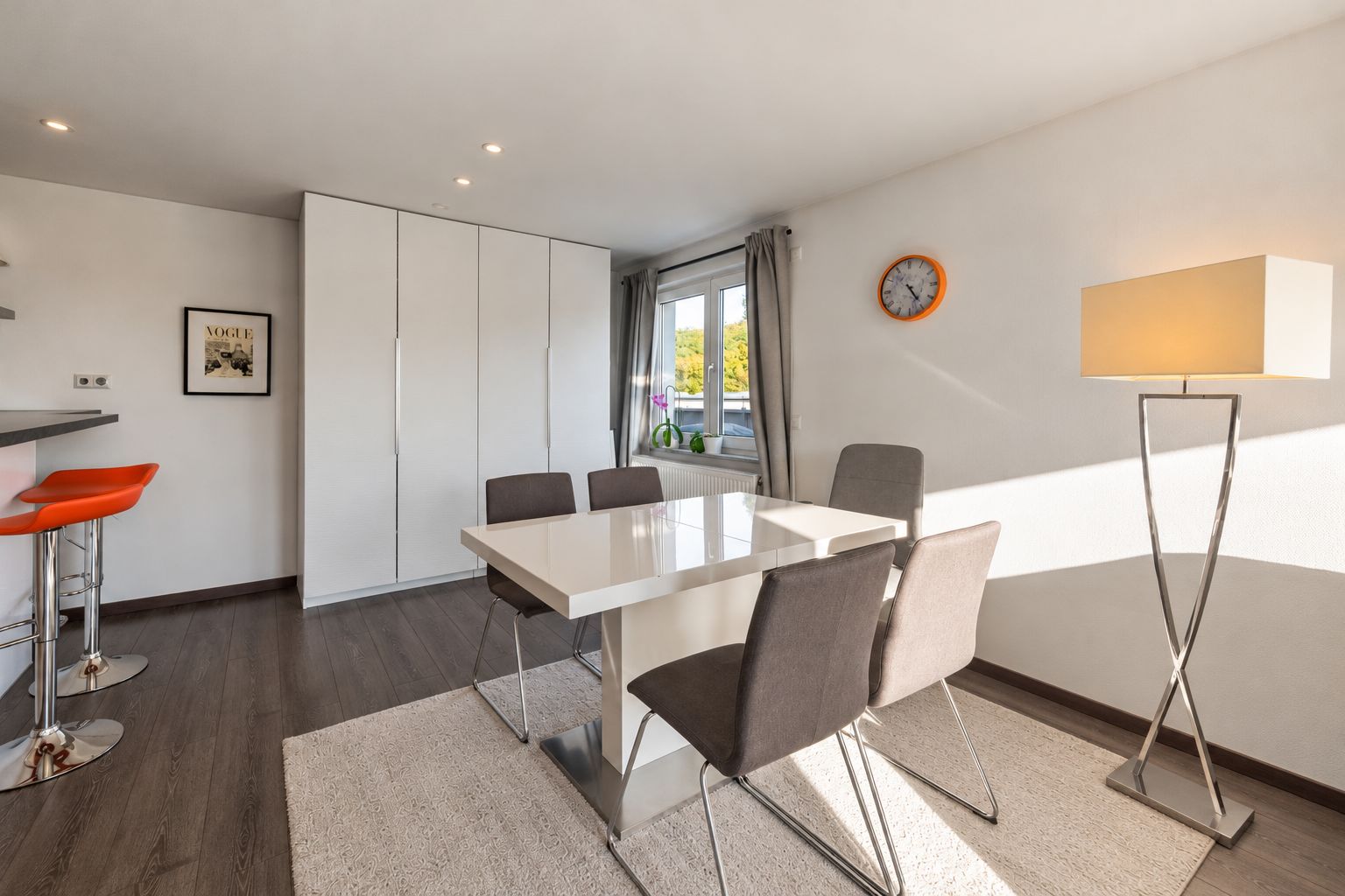 Essbereich mit weißem Tisch, vier Stühlen, Stehlampe und großem weißen Schrank.