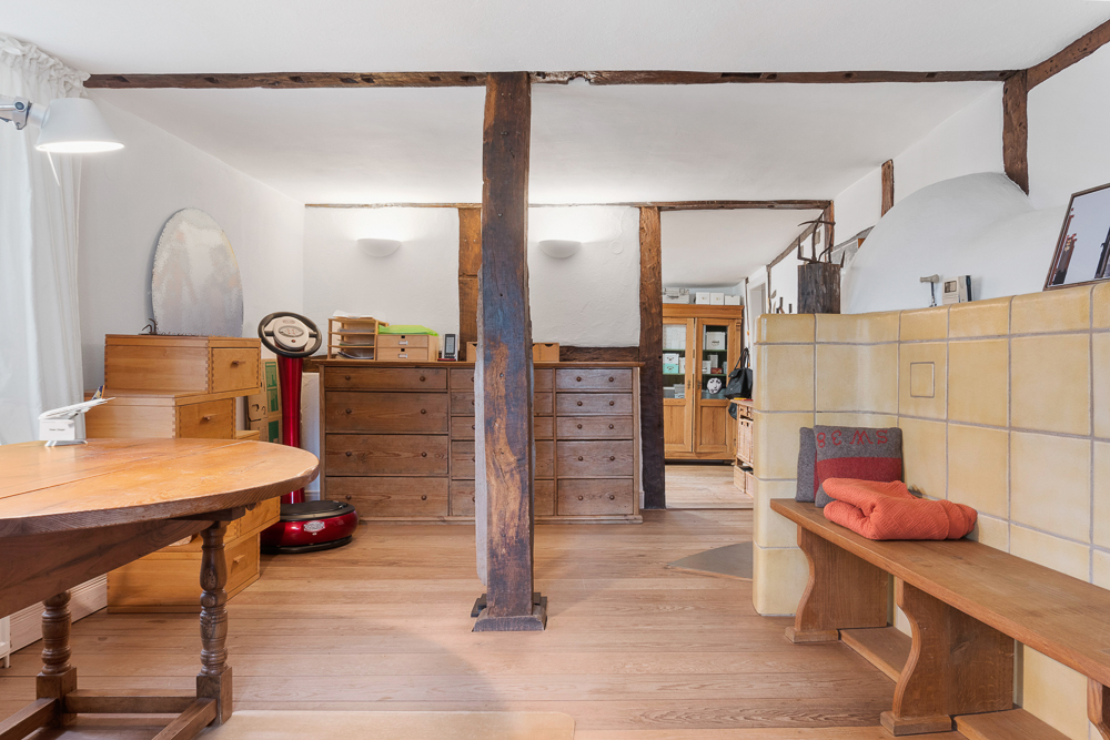 Heller Wohnraum mit Holzboden, Holzmöbeln, Bank und einem gelben Kachelofen.