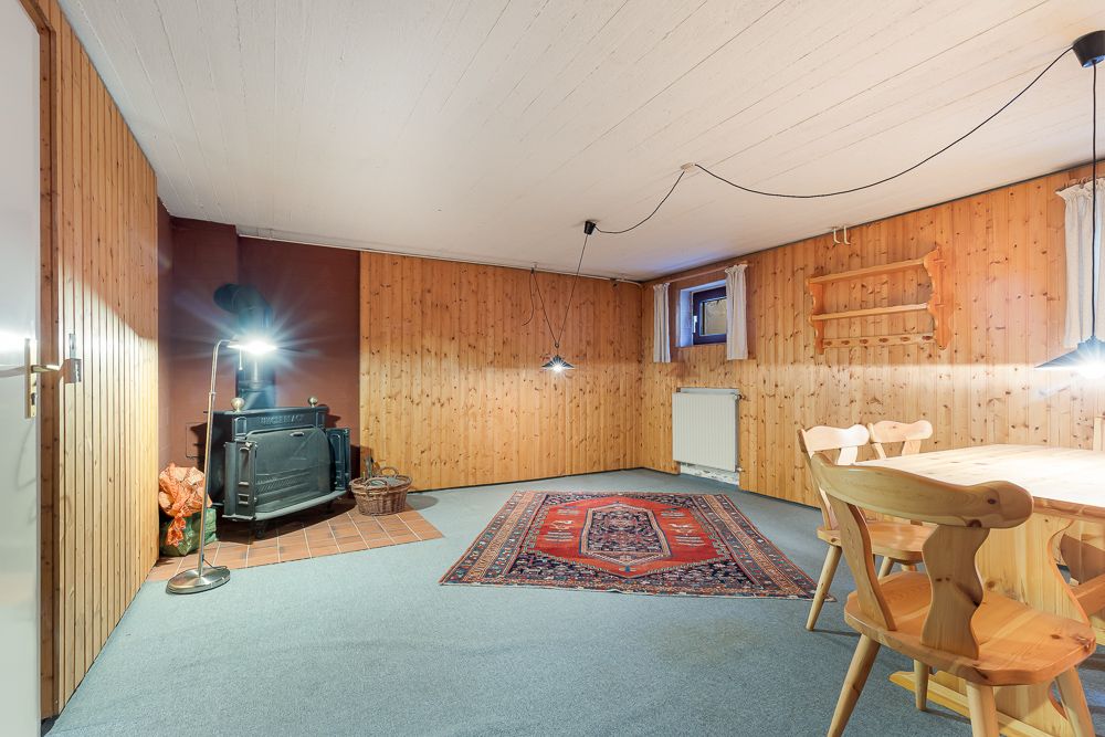 Wohnzimmer mit Holzwänden, Teppich, Holzofen, Esstisch und Holzstühlen.
