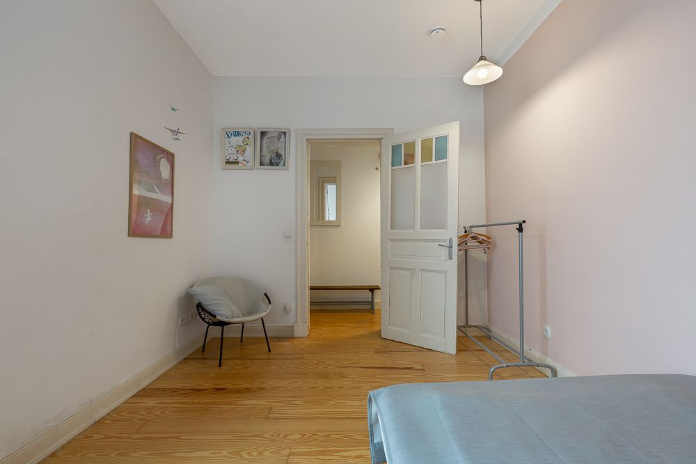 Helles Schlafzimmer mit Holzboden, Stuhl, Wandbildern und offener Tür.