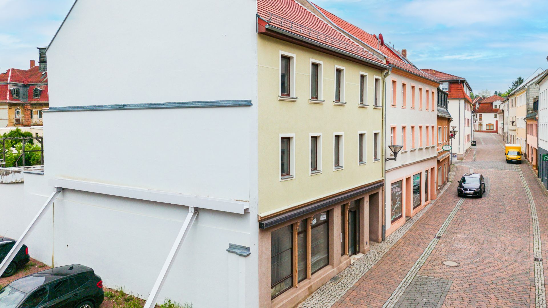 Wohnhaus mit gelber Fassade an einer gepflasterten Straße, mehrere Fenster und Eingänge sichtbar.