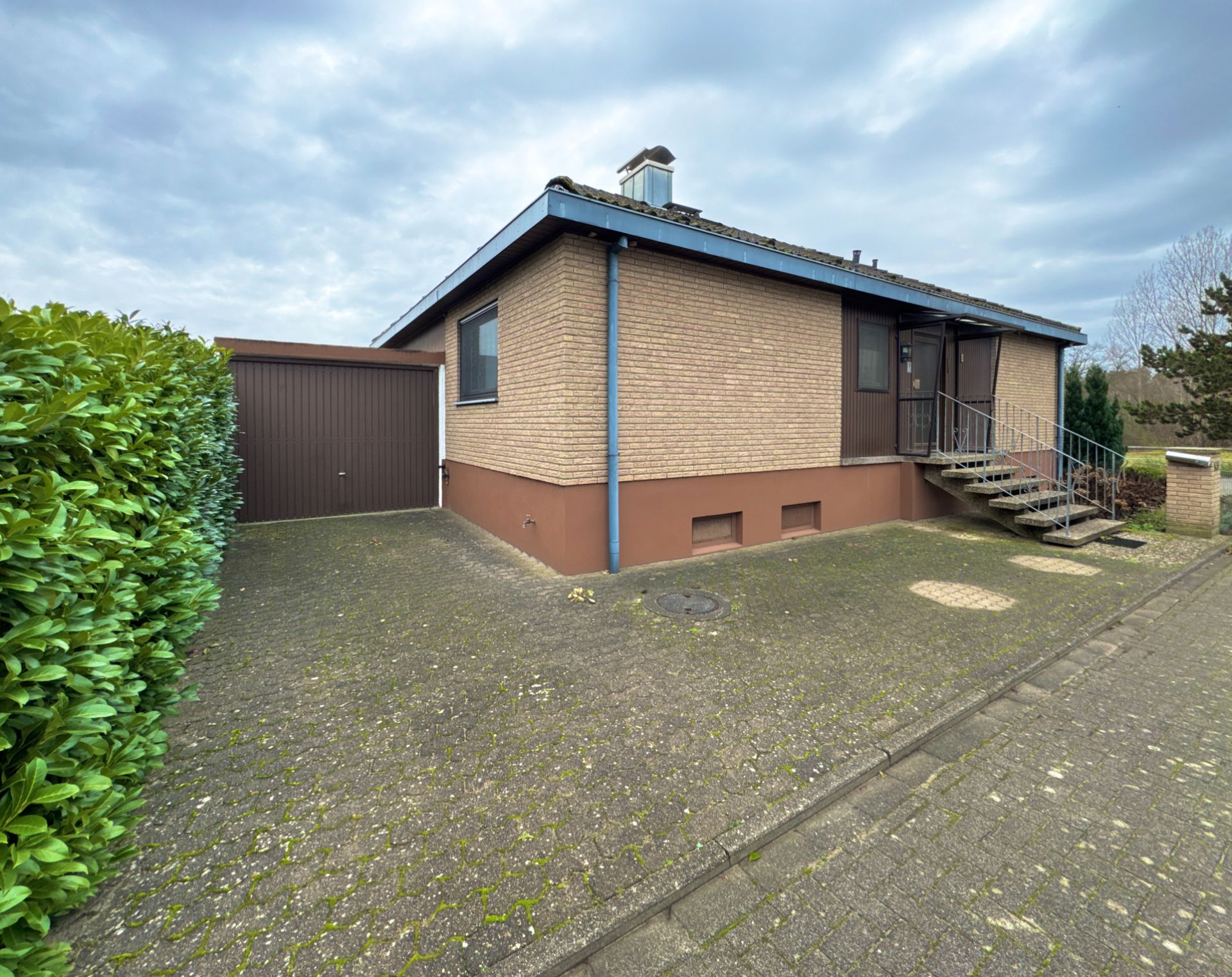 Einfamilienhaus mit Garage, gepflasterter Einfahrt und seitlichem Treppenaufgang.