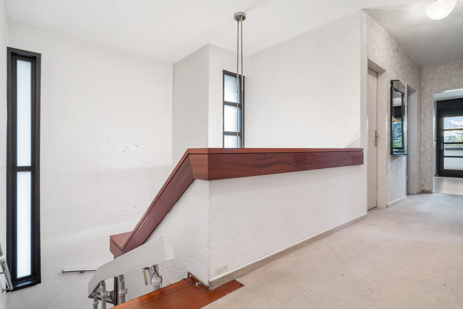 Heller Flur mit Treppe und Fenstern, Teppichboden und weißen Wänden.
