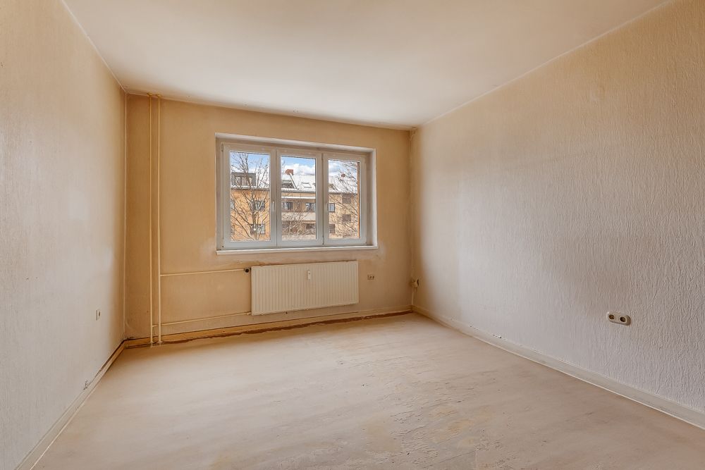 Leerer Raum mit beigem Boden, großem Fenster und Heizkörper unter dem Fenster.