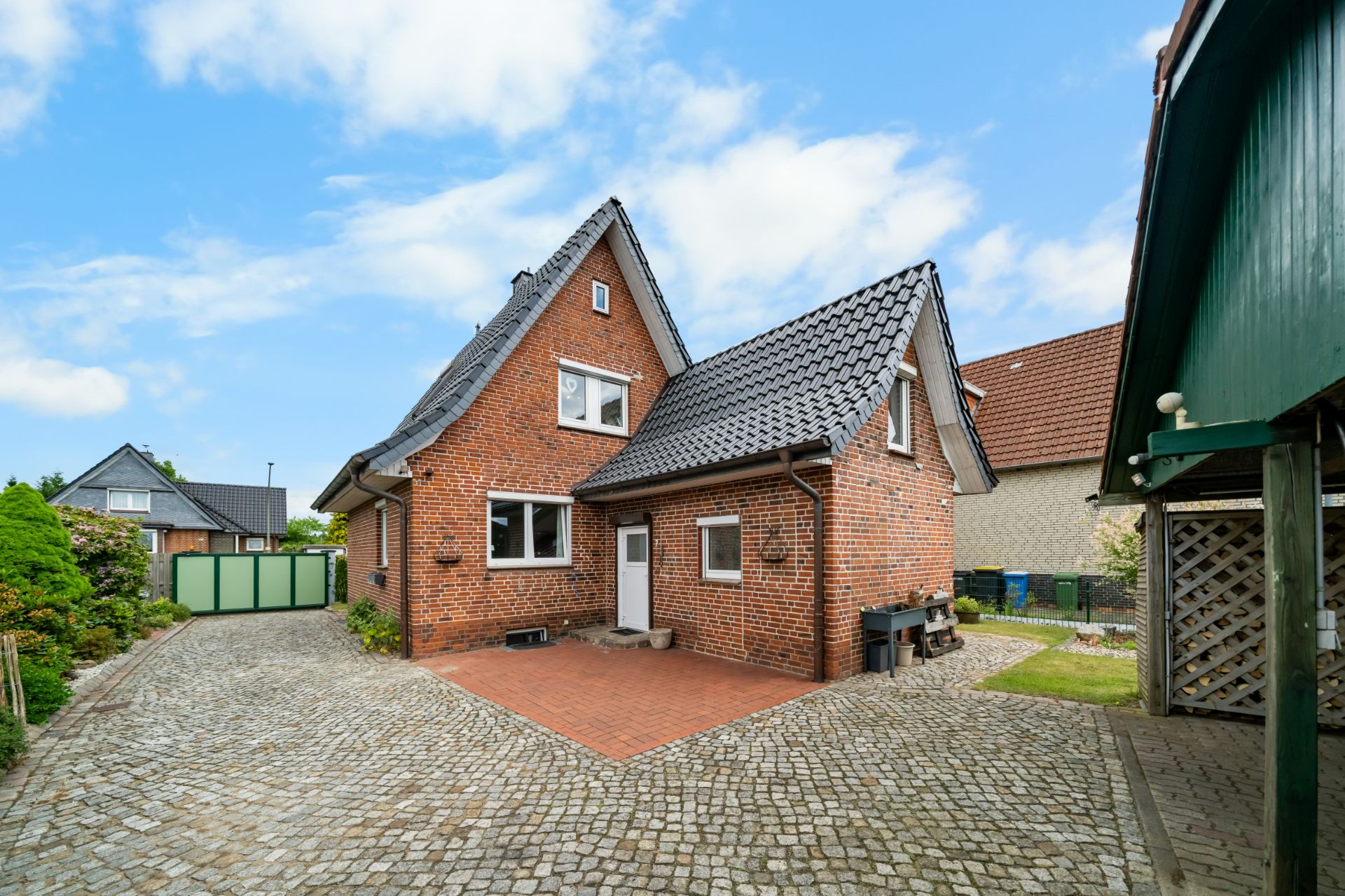 Backsteinwohnhaus mit dunklem Dach, gepflastertem Hof und seitlichem Gartenbereich.