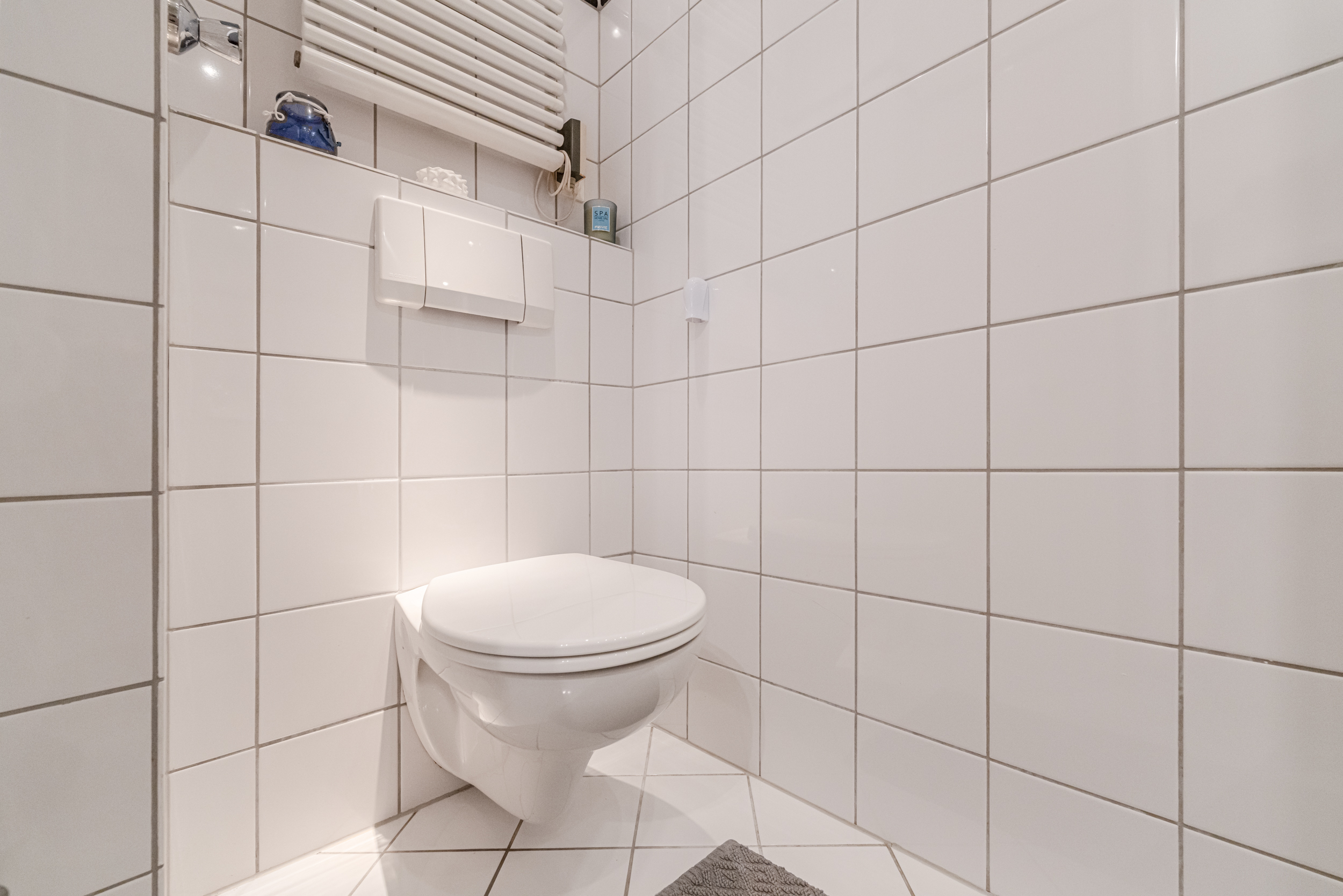 Modernes, weiß gefliestes Badezimmer mit wandhängender Toilette und Heizkörper.
