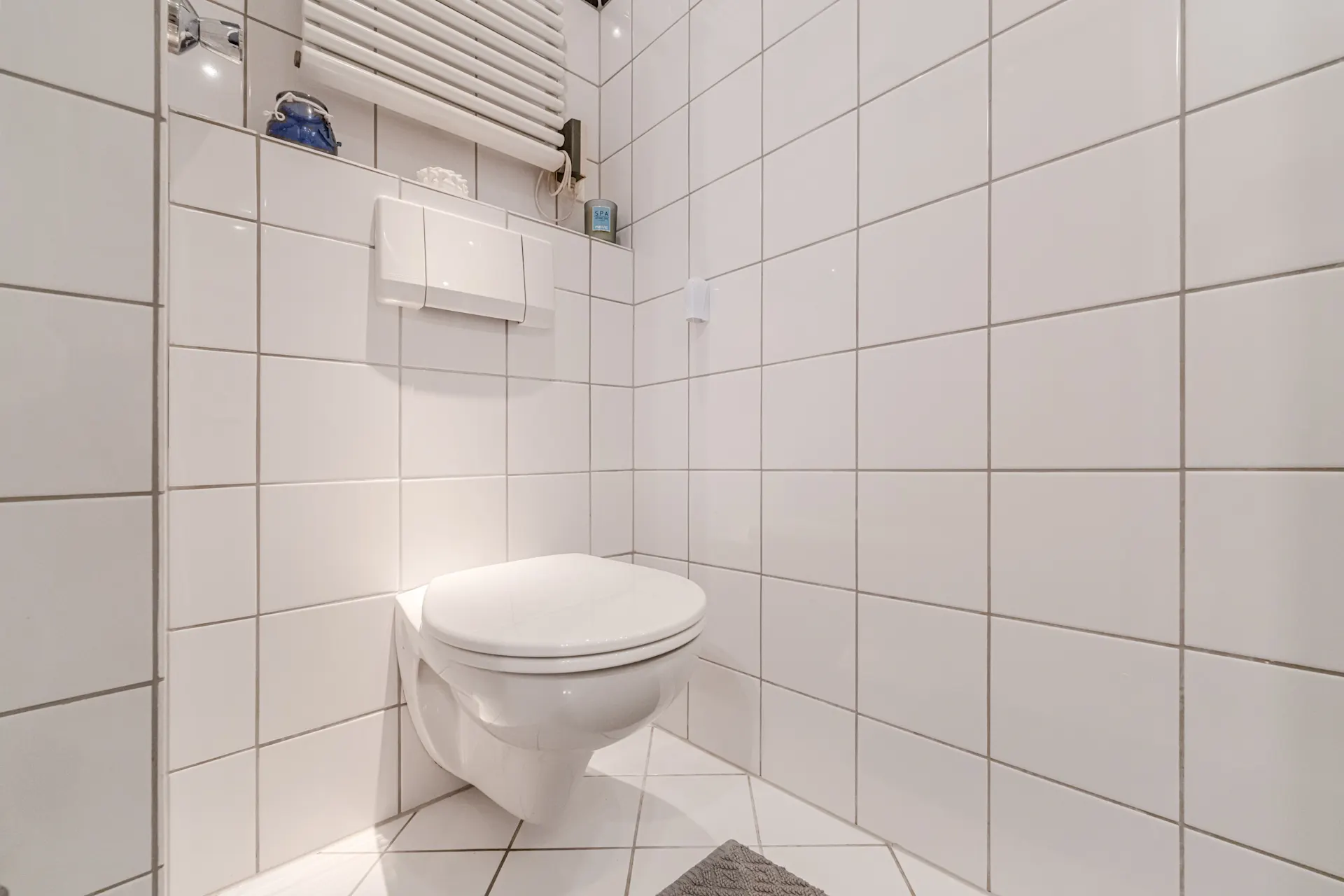 Modernes, weiß gefliestes Badezimmer mit wandhängender Toilette und Heizkörper.